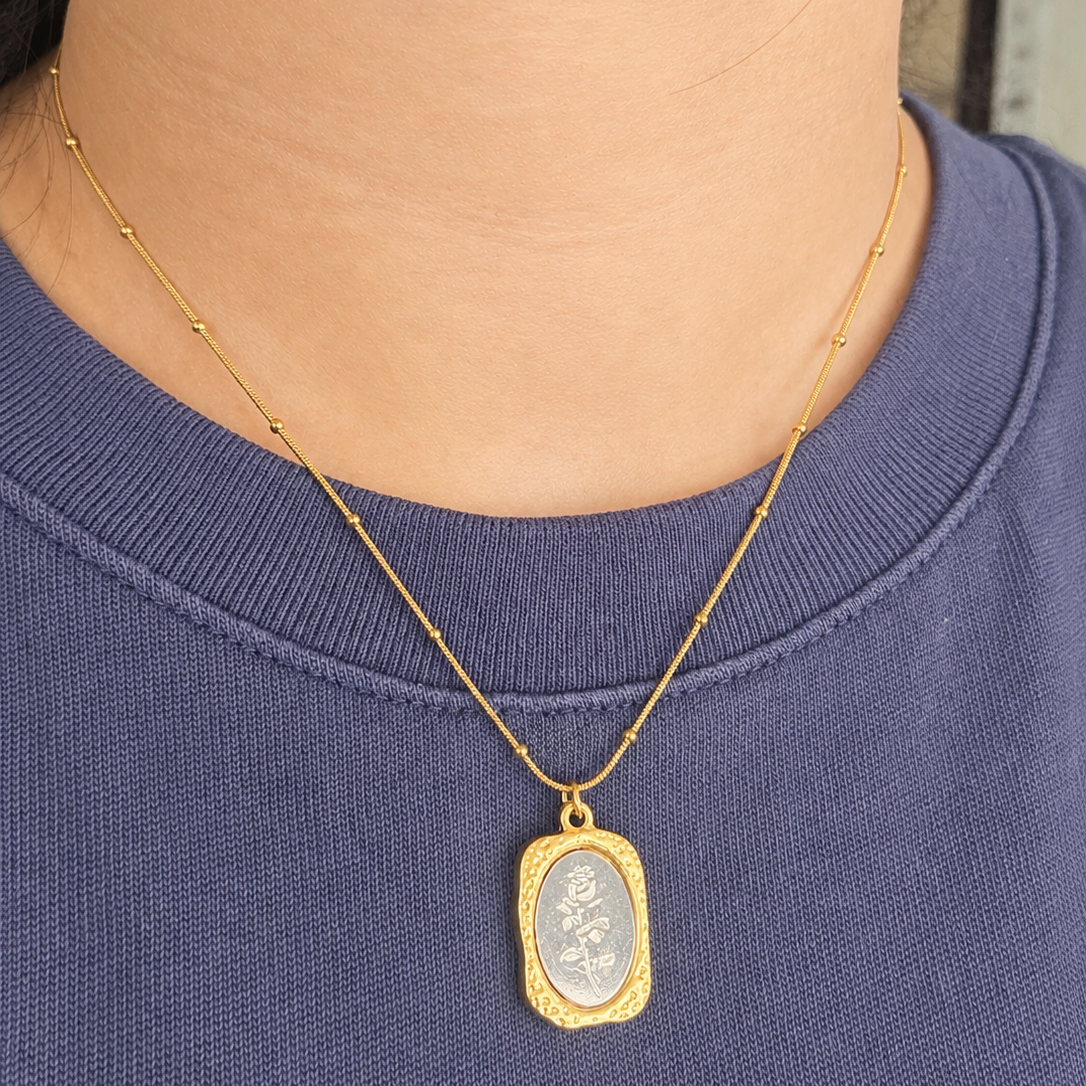 Gold necklace with a pendant on a person wearing a blue shirt