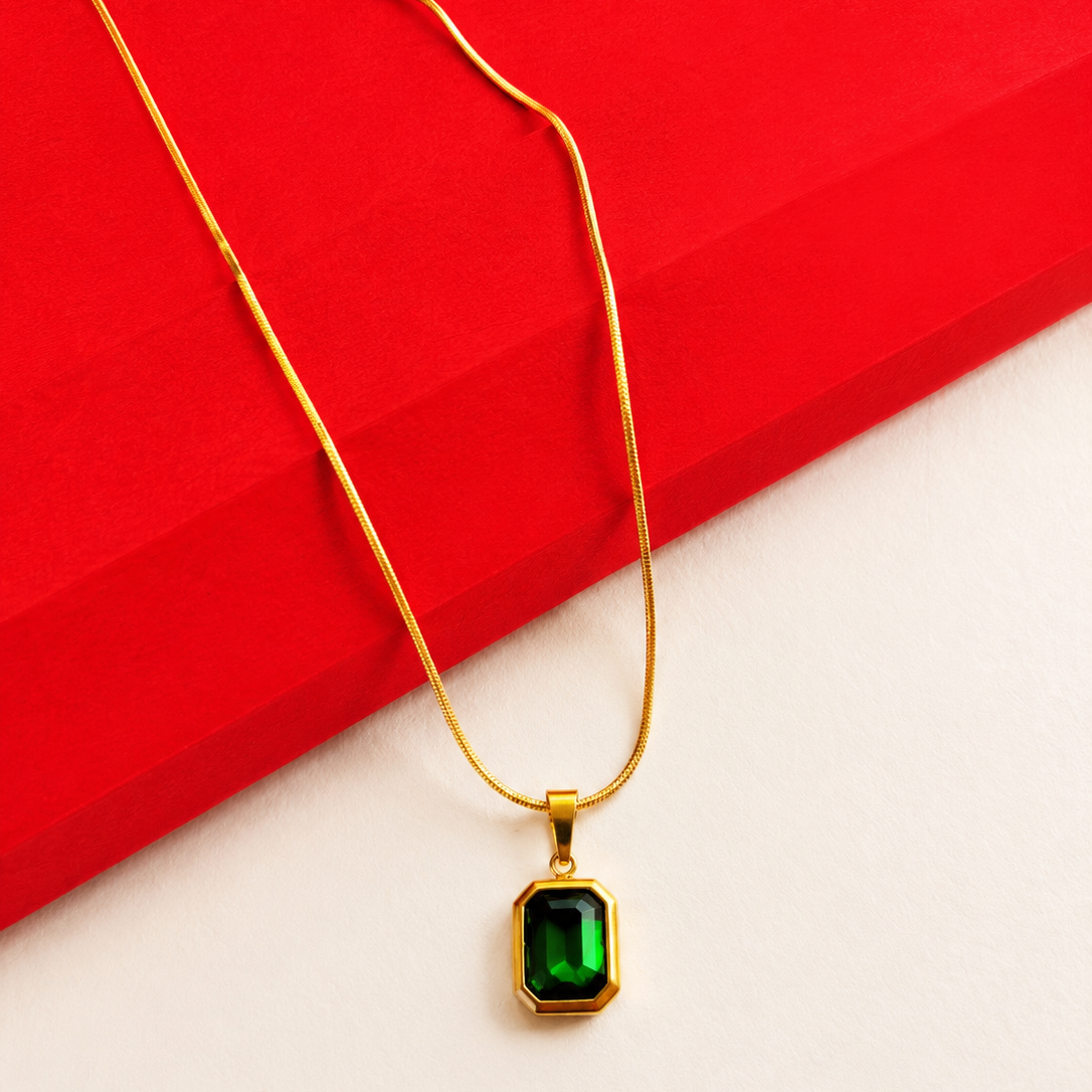 Gold necklace with a green gemstone pendant on a red and white background