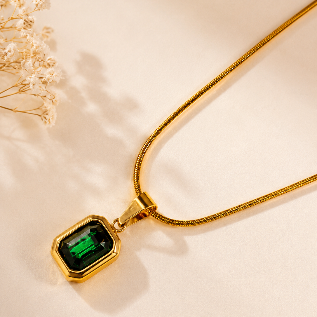 Gold necklace with a green gemstone pendant on a beige background