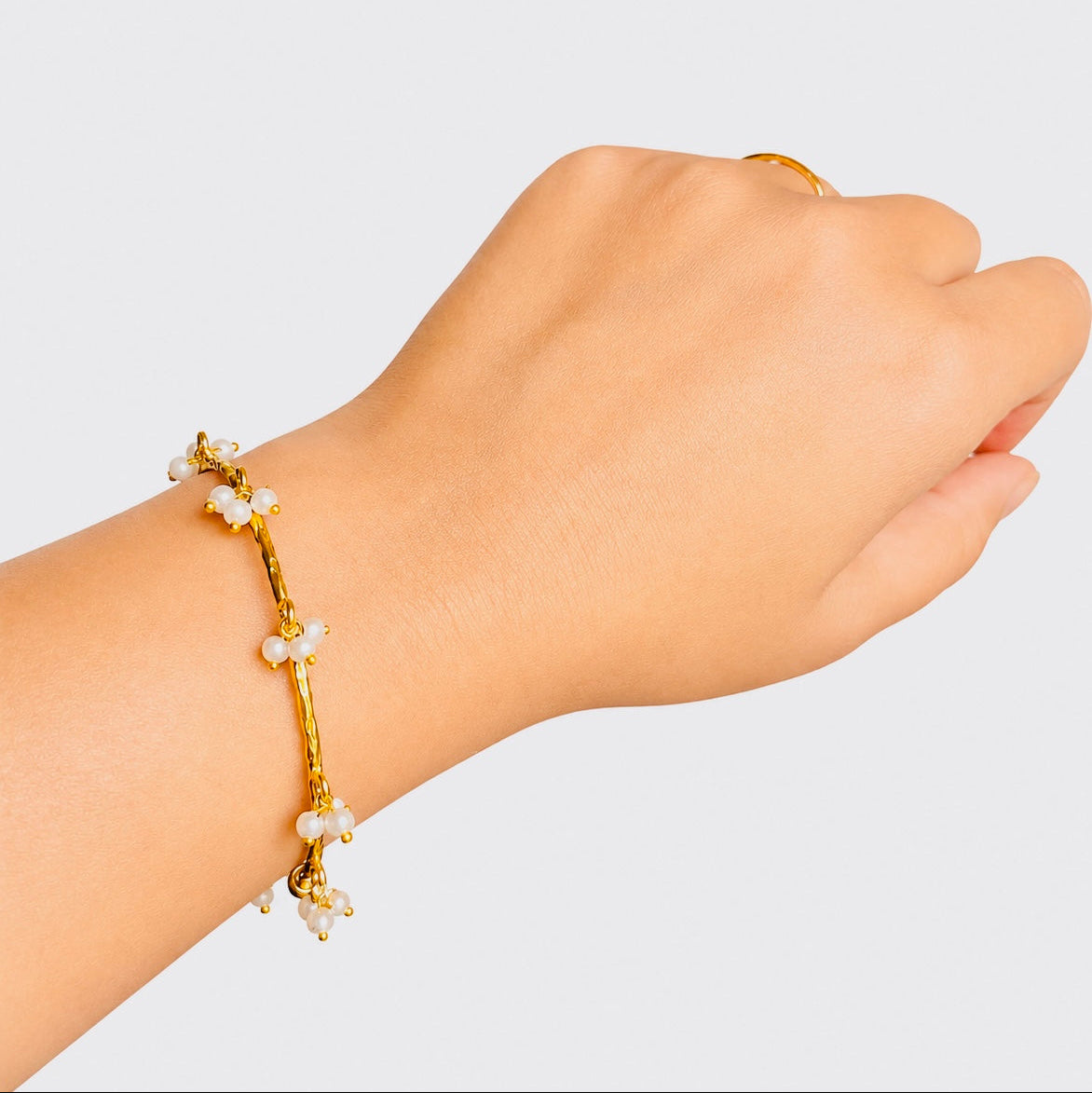Gold bracelet with small pearls on a wrist against a light gray background