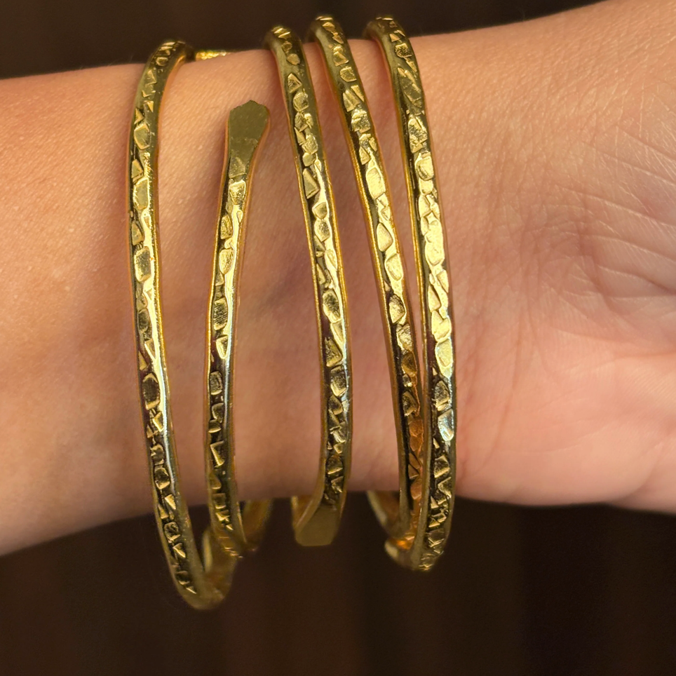 Gold bangles on a wrist against a dark background