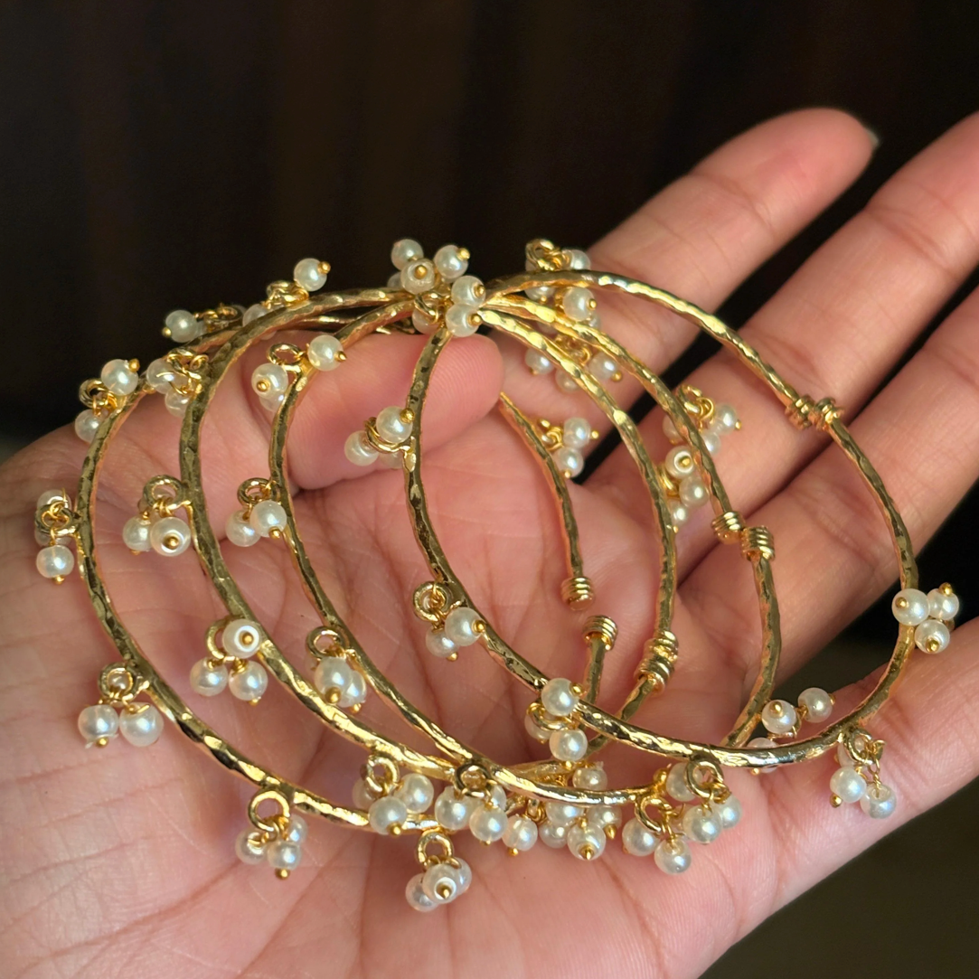 Gold bangles with pearl beads on a hand against a dark background