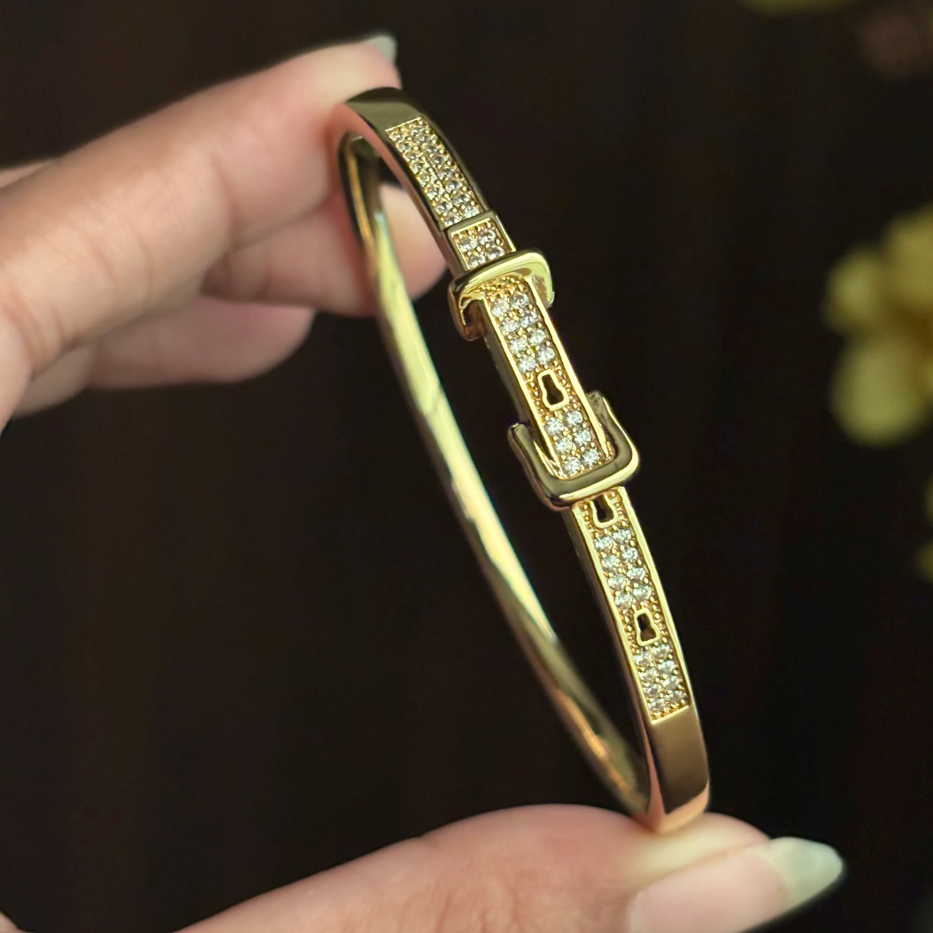 Gold bracelet with diamond accents held by a hand against a dark background
