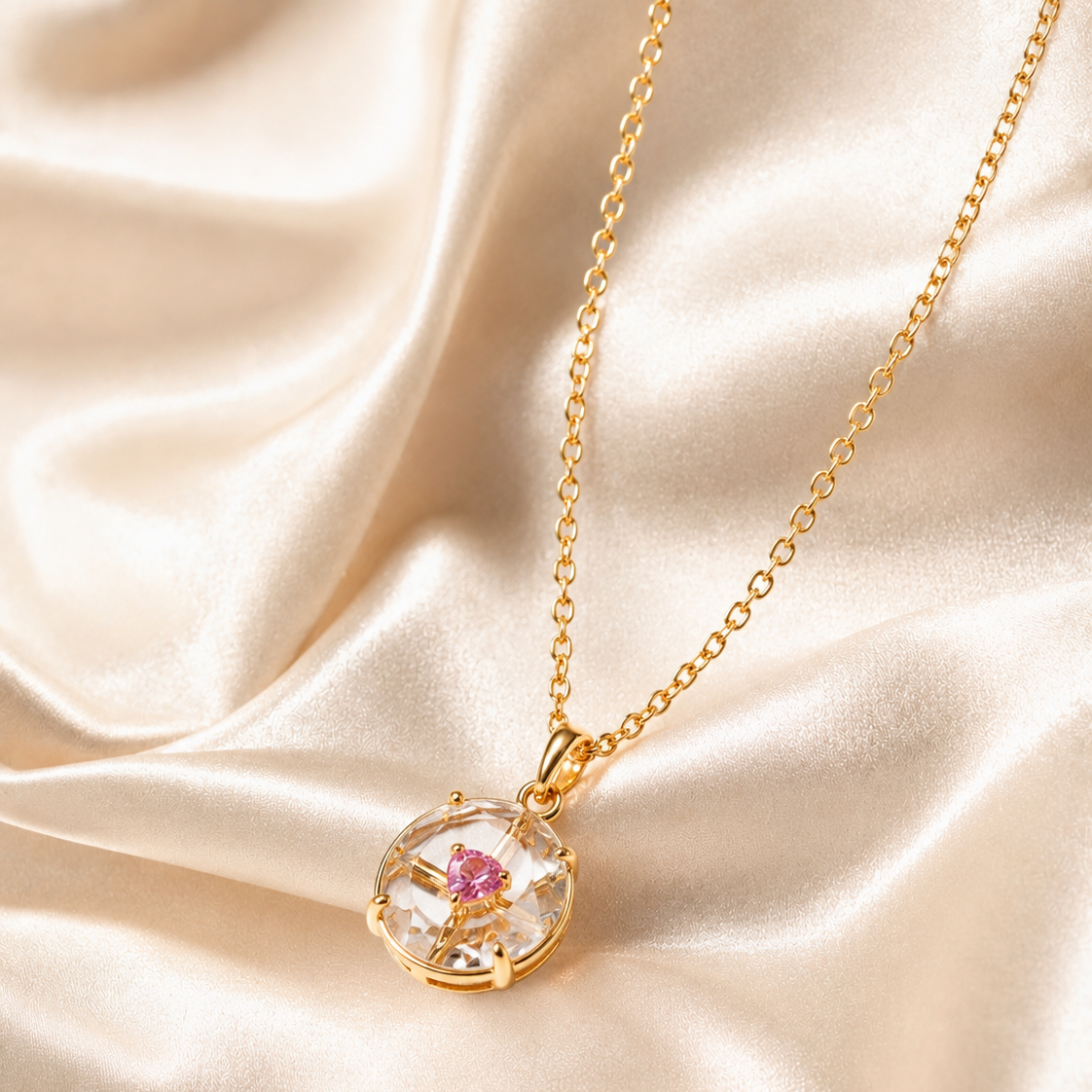 Gold necklace with a clear pendant featuring a pink gemstone on a beige satin background