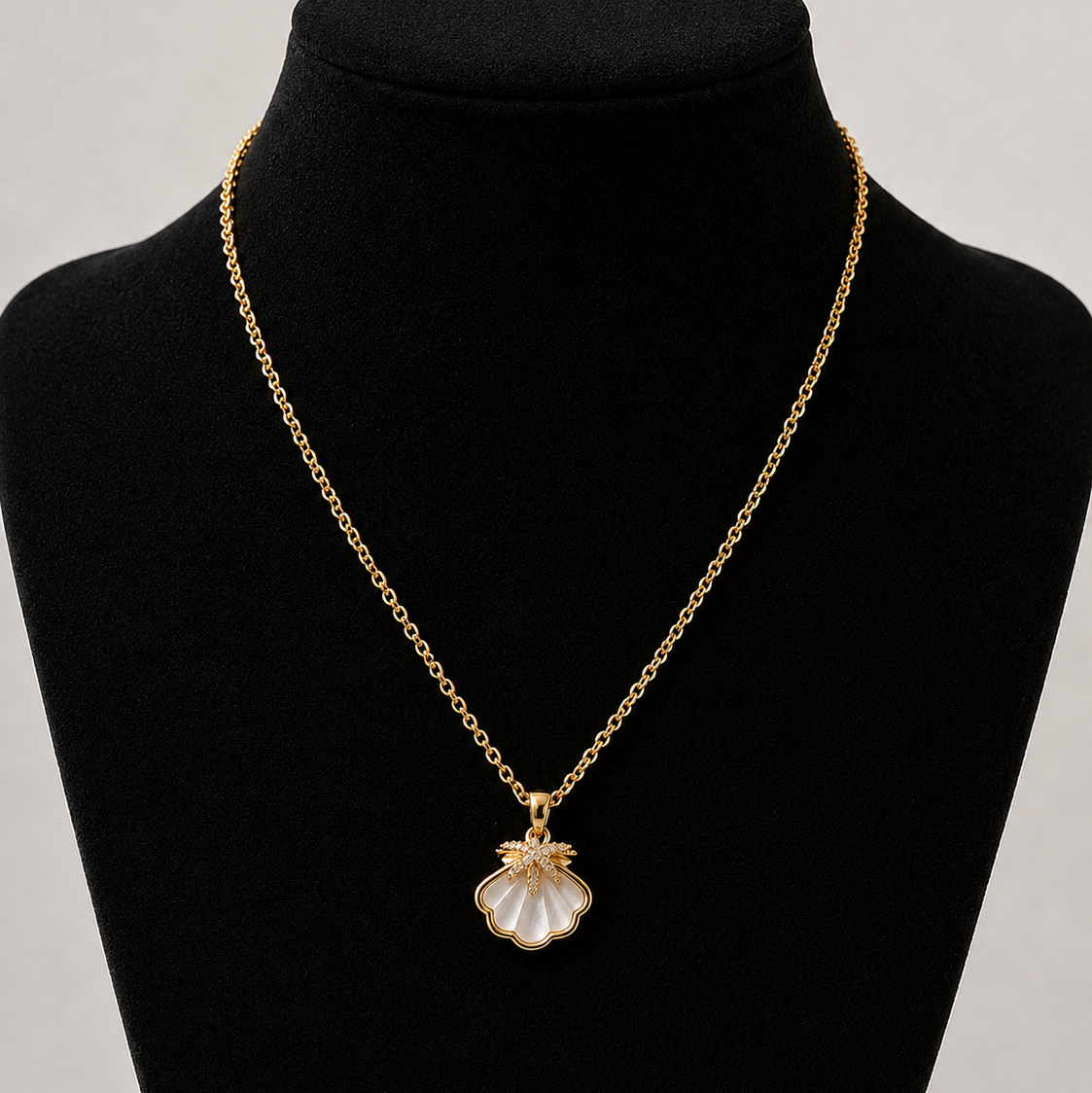 Gold necklace with a shell pendant on a black mannequin bust against a gray background