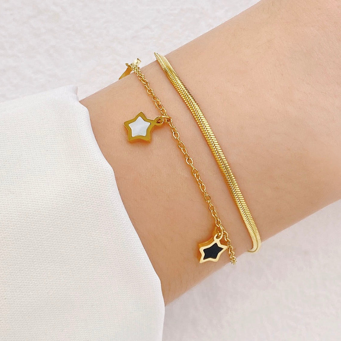 Gold bracelet with star-shaped charms on a wrist against a white background