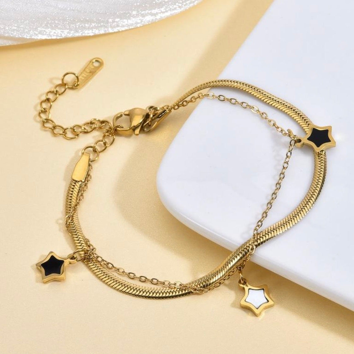 Gold bracelet with star-shaped charms on a white and beige background