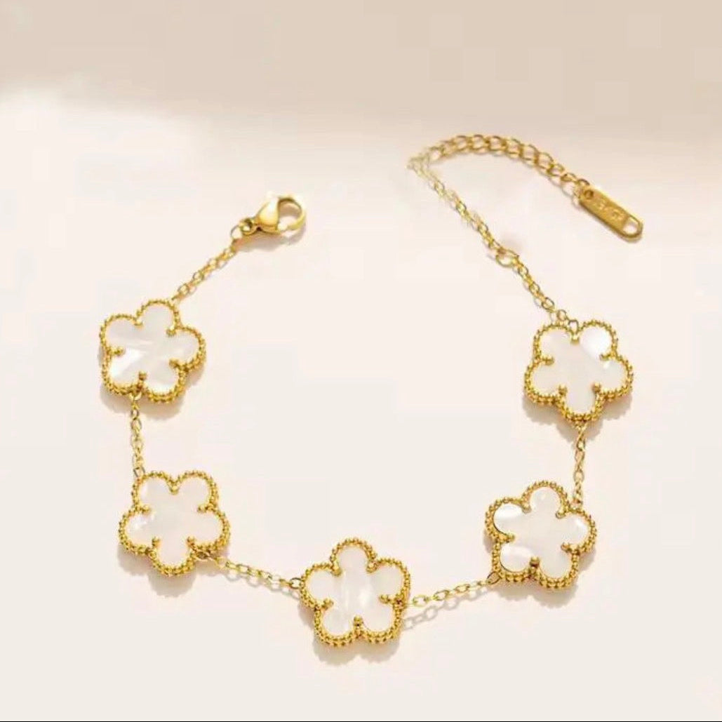 Gold bracelet with white clover-shaped charms on a light background
