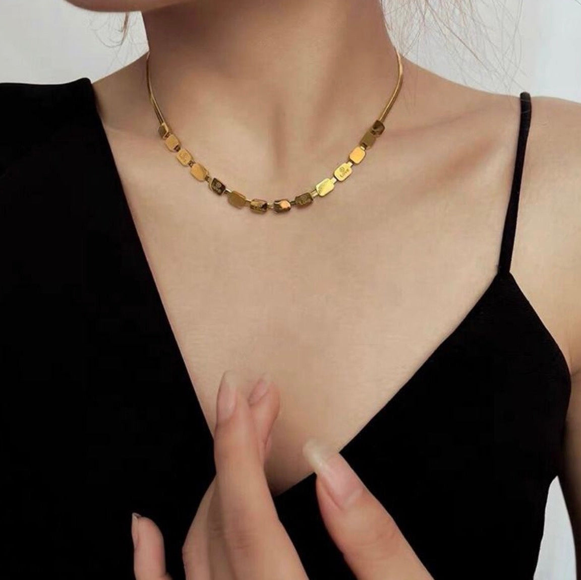 Gold necklace being worn by a person with a plain background