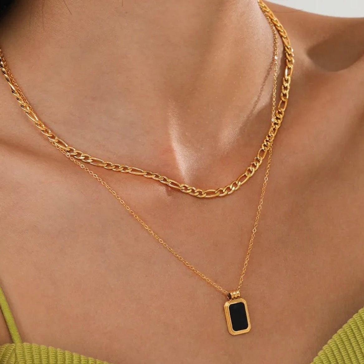 Gold chain necklace with a pendant on a person wearing a green top.
