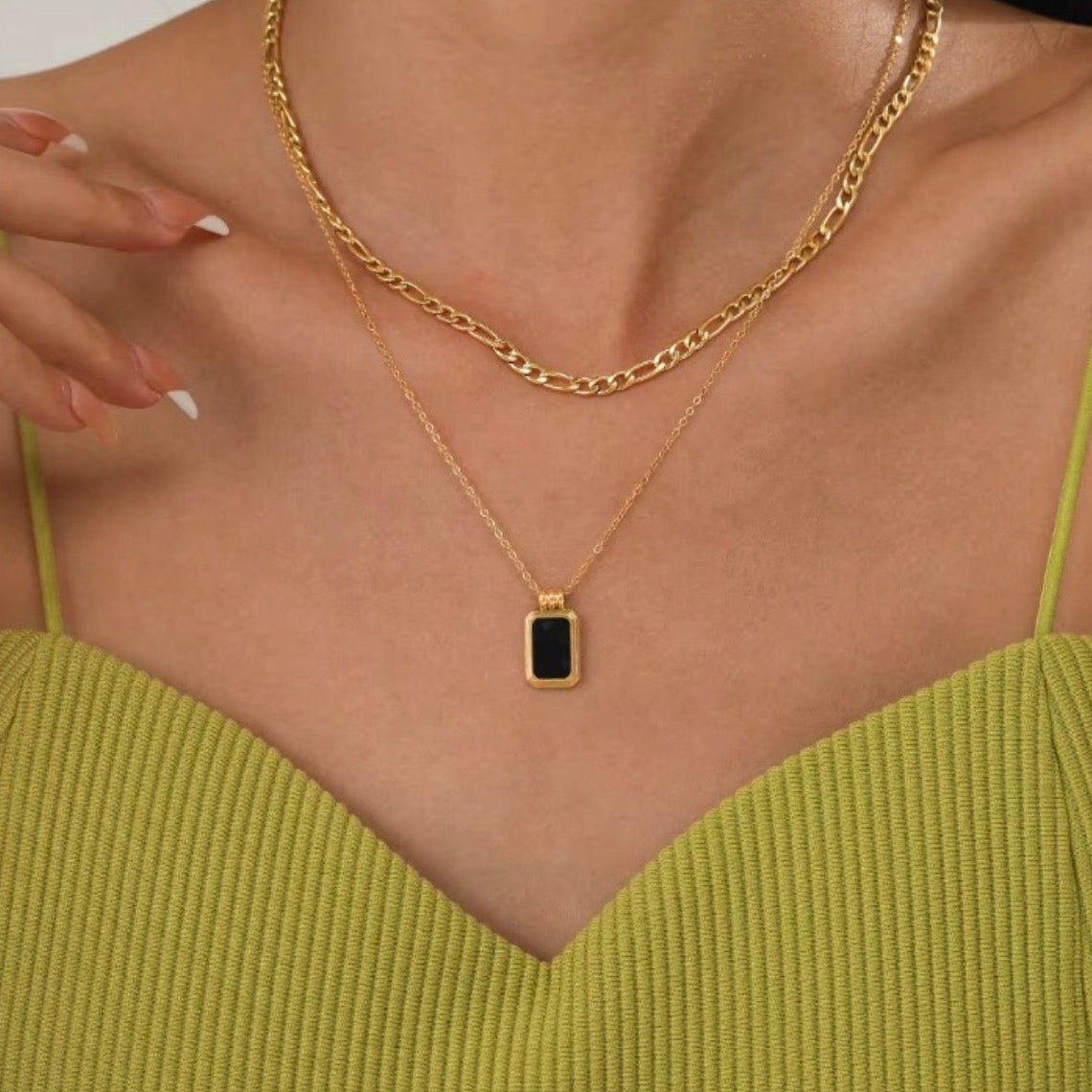 Gold necklace with a pendant on a person wearing a green top.