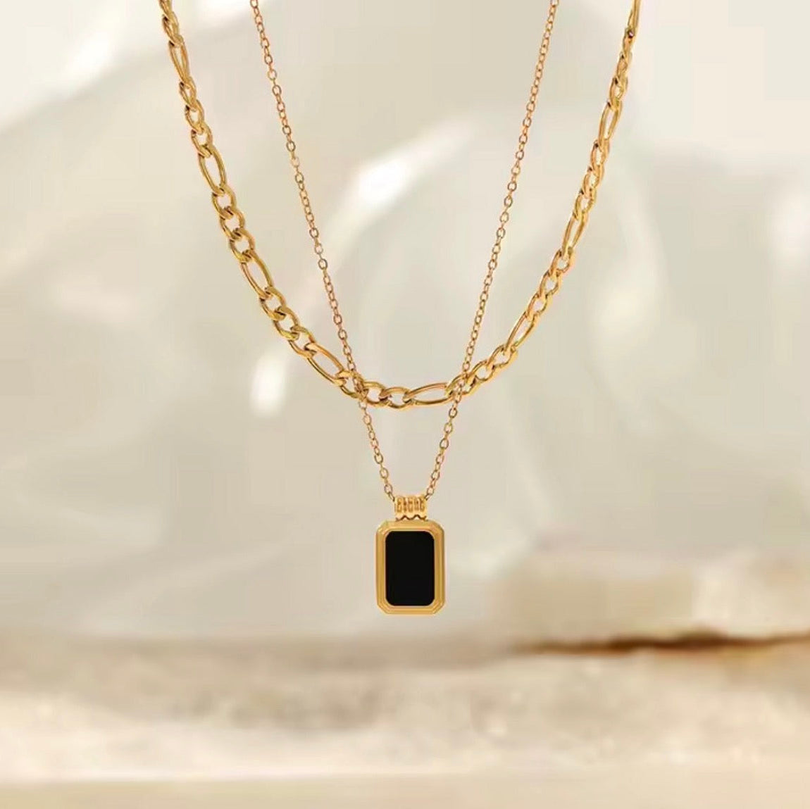 Gold necklace with a black pendant on a light background