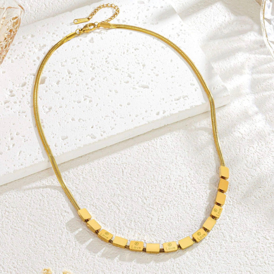 Gold necklace with engraved beads on a textured white surface