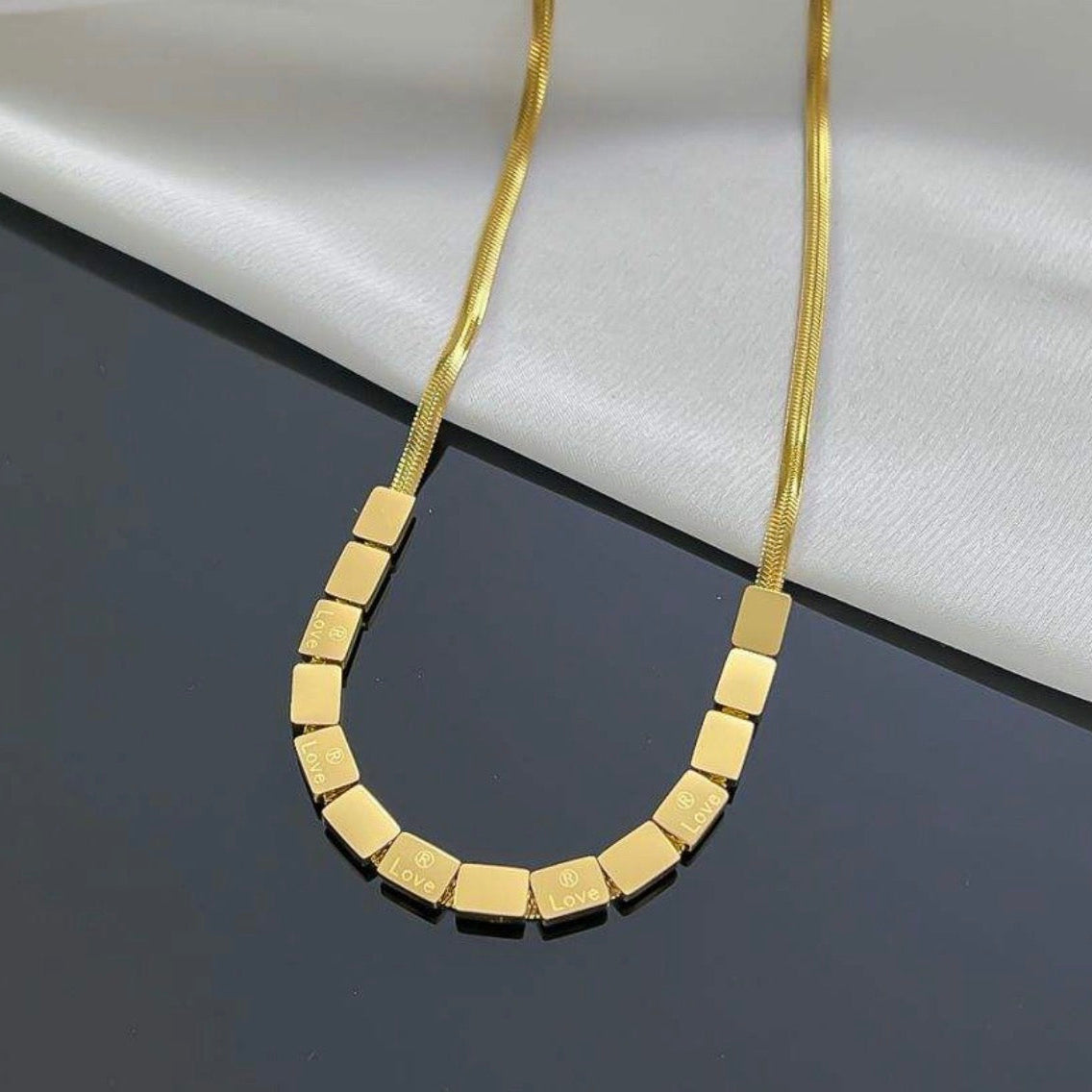 Gold necklace with square links on a dark surface