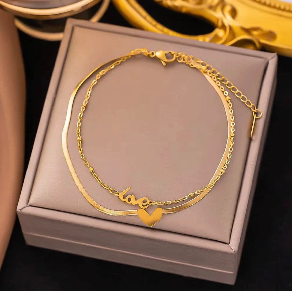 Gold bracelet with 'love' and heart charm on a gray box
