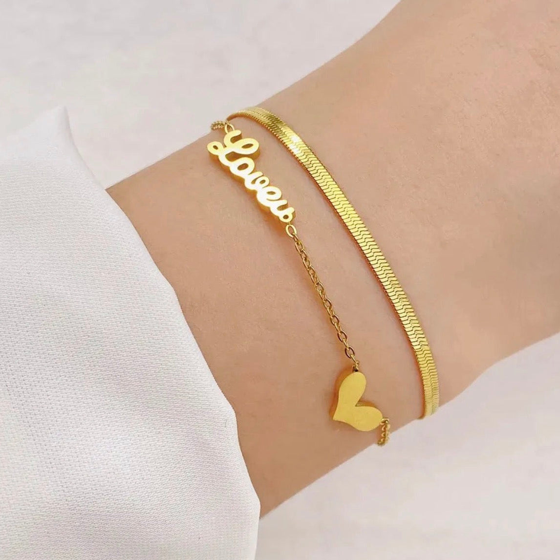 Gold bracelet with 'Loves' and heart charm on a wrist against a white background