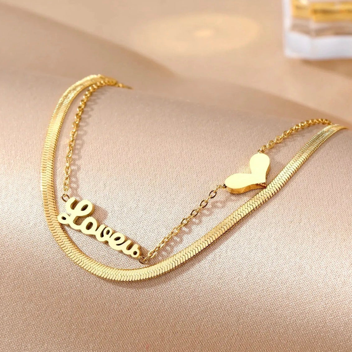Gold necklace with 'Love' pendant on a beige surface