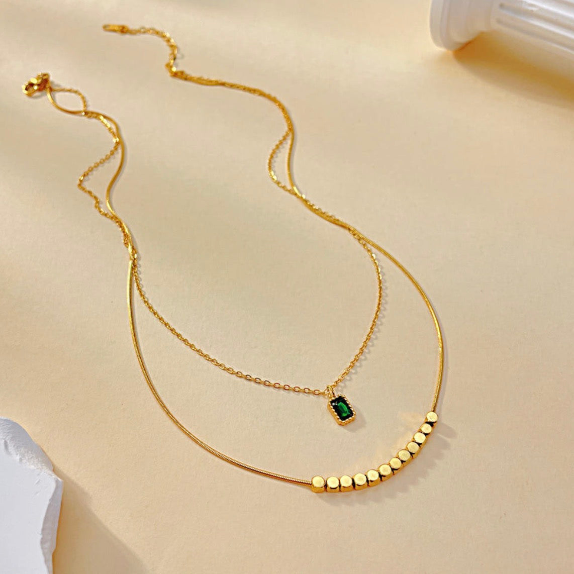 Gold necklace with a green gemstone on a beige background