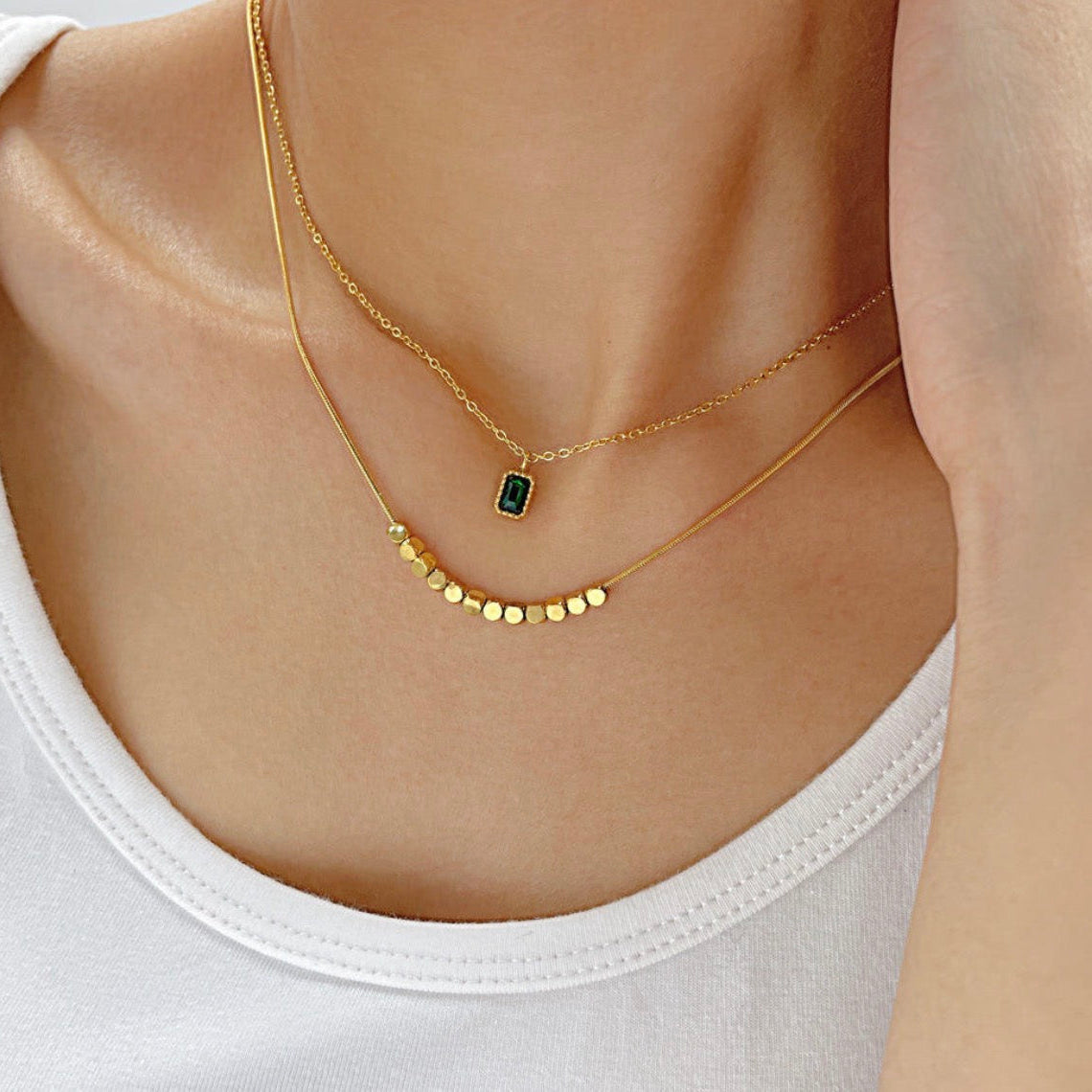 Gold necklace with a green gemstone on a person wearing a white tank top.