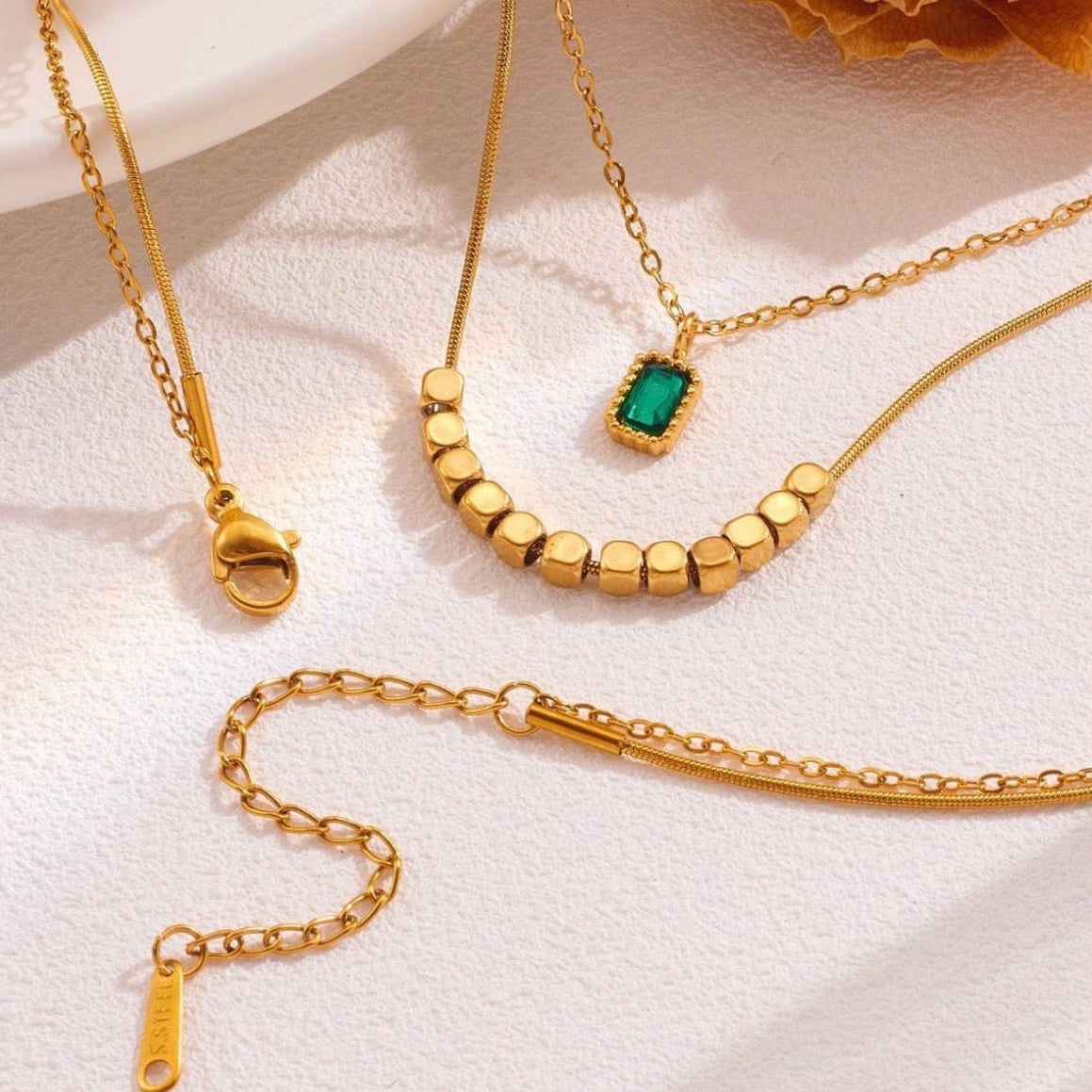 Gold necklaces with a green gemstone on a white surface