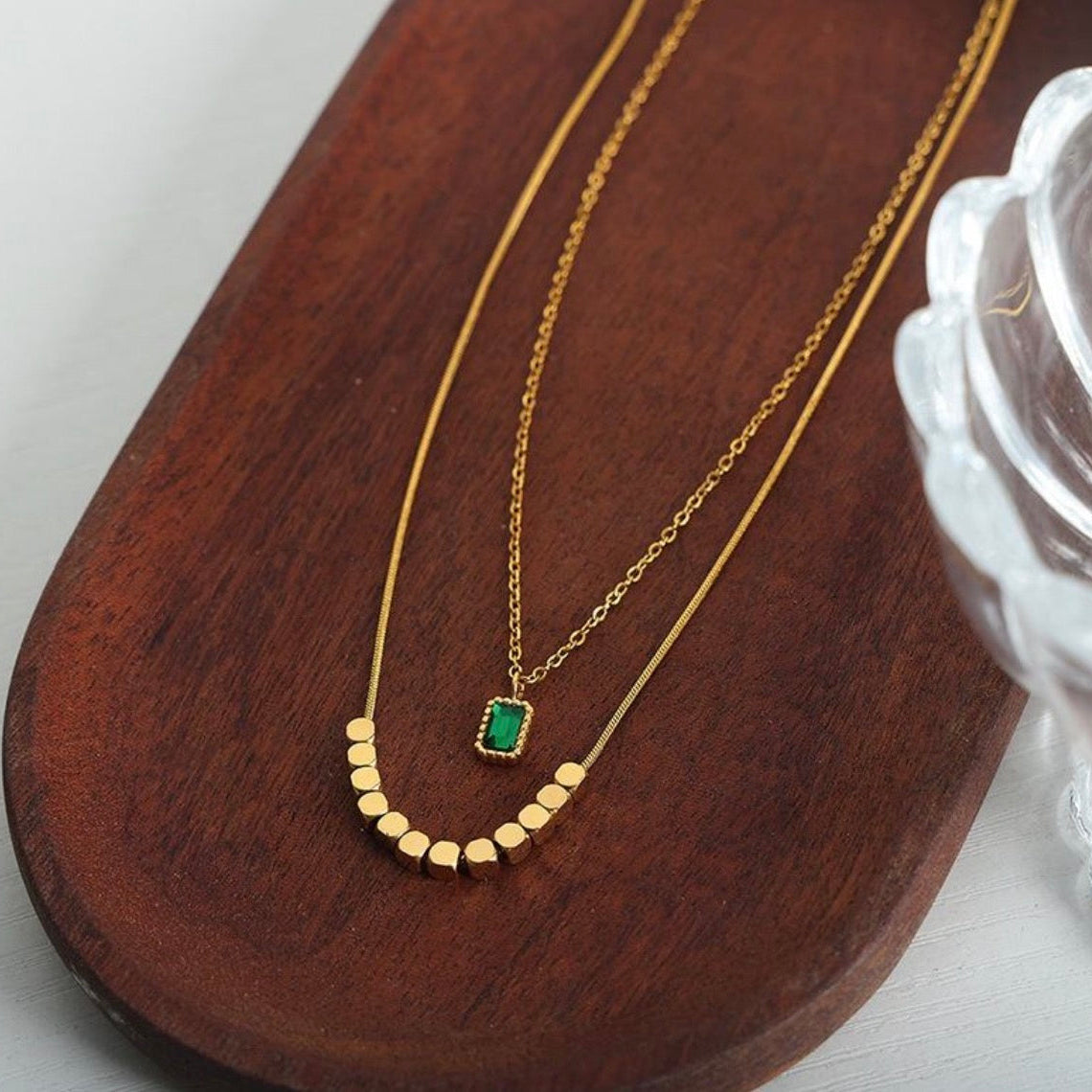 Gold necklace with a green gemstone pendant on a wooden surface