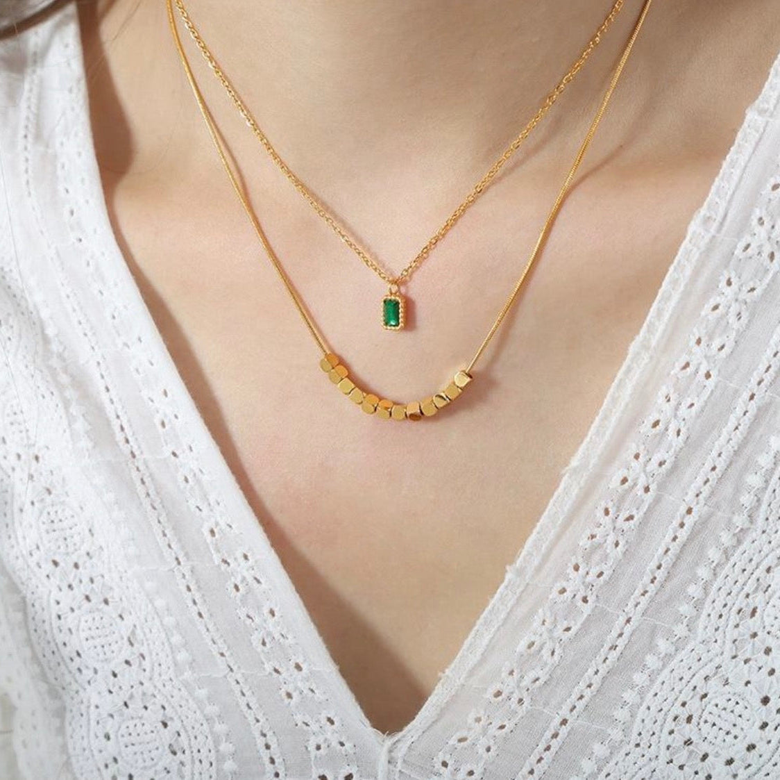 Gold necklace with a green gemstone pendant on a white blouse
