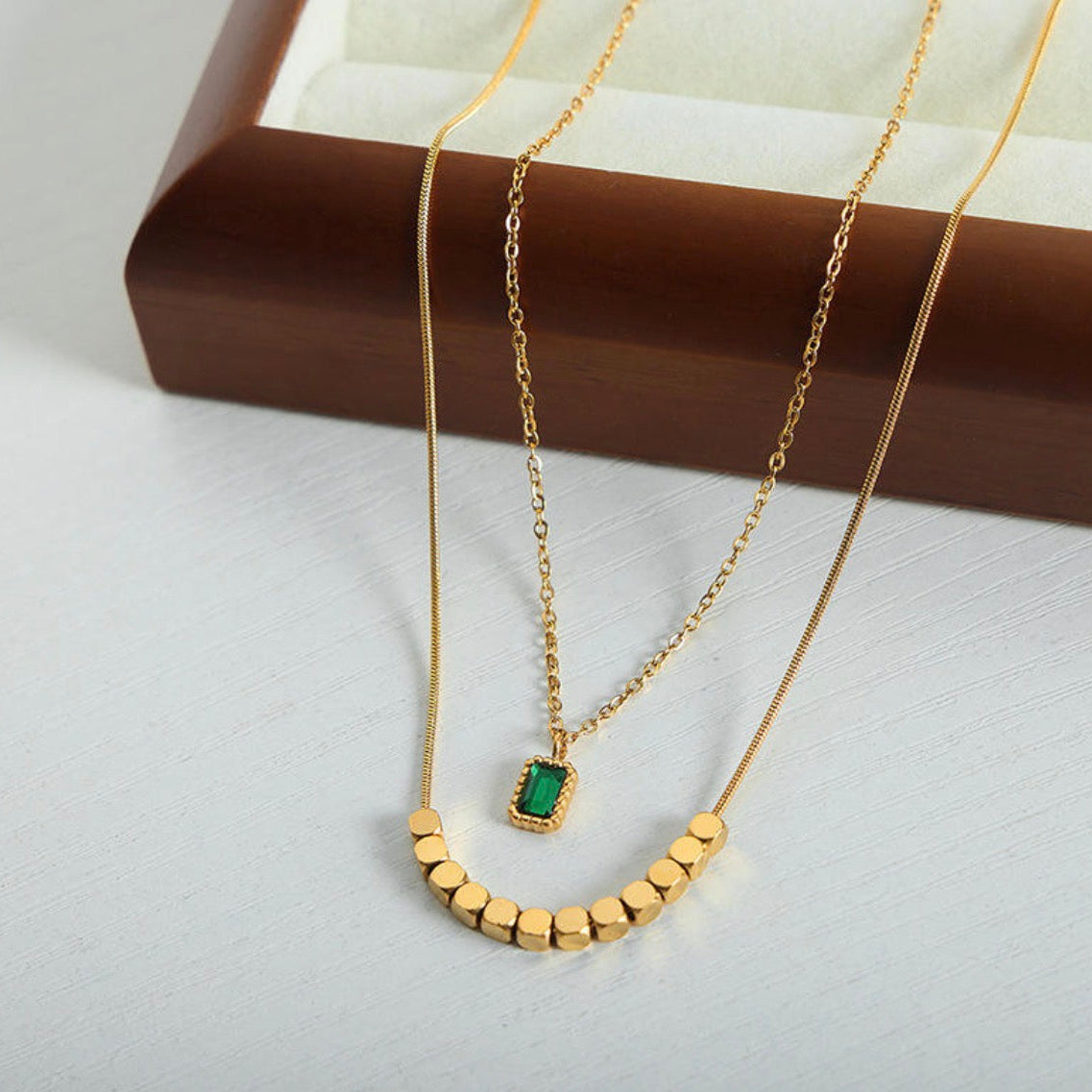 Gold necklace with a green gemstone pendant on a white surface