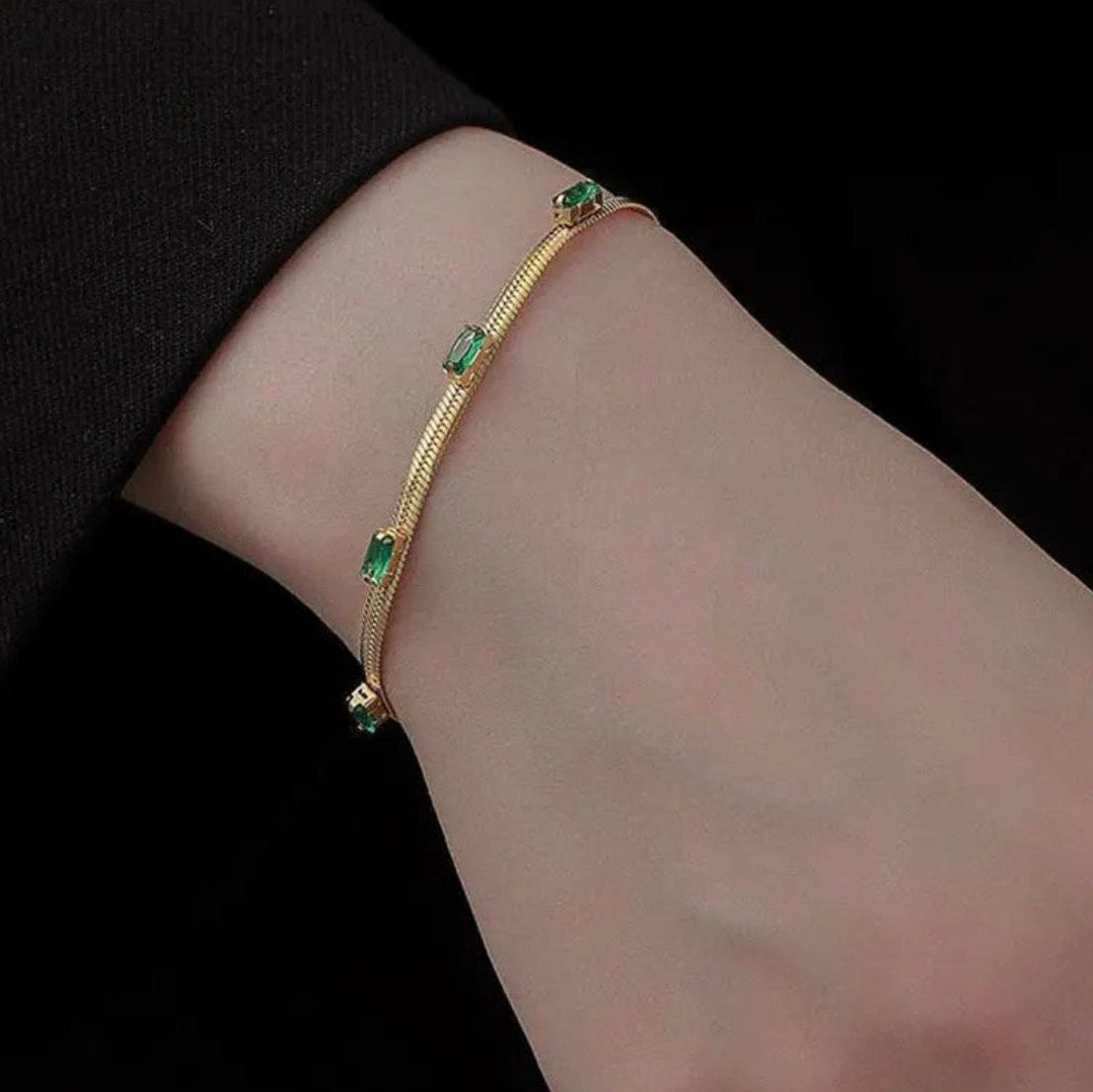 Gold bracelet with green gemstones on a wrist against a black background