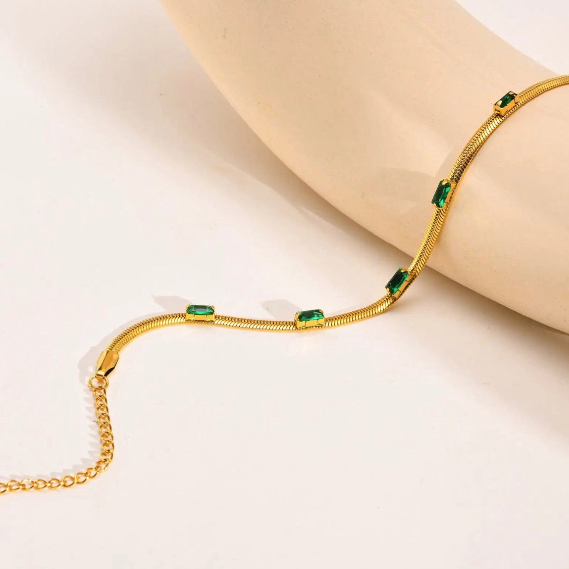 Gold bracelet with green gemstones on a beige background