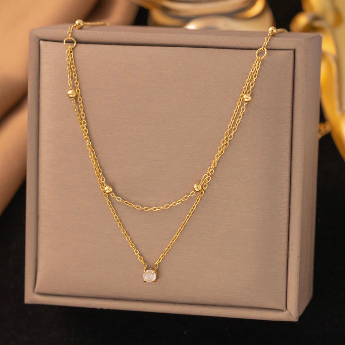 Gold necklace with a small gemstone on a beige jewelry box
