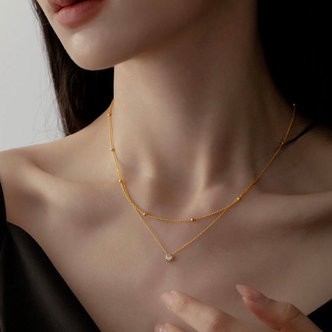 Close-up of a person wearing a gold necklace with a small gemstone on a neutral background