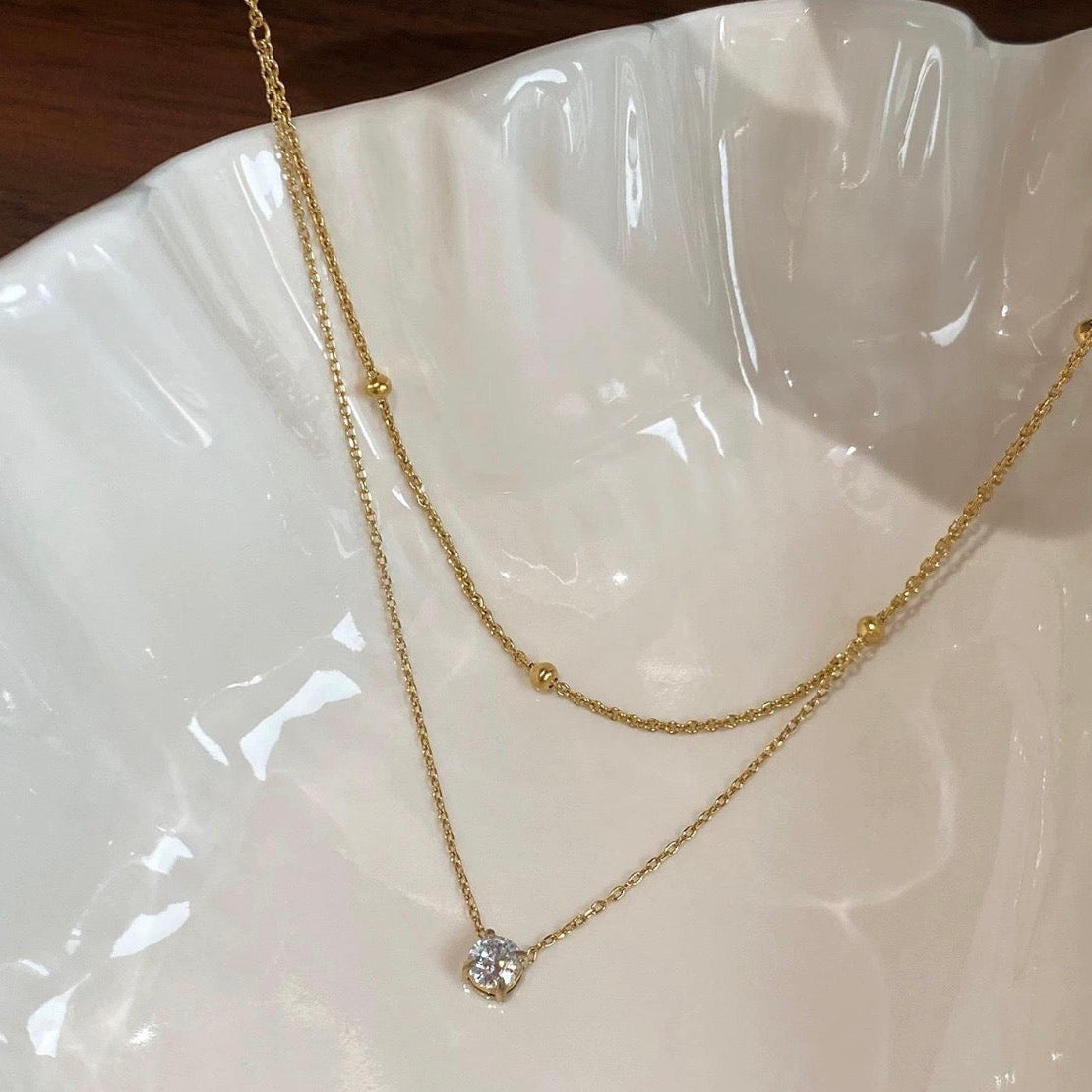 Gold necklace with a diamond pendant on a white dish