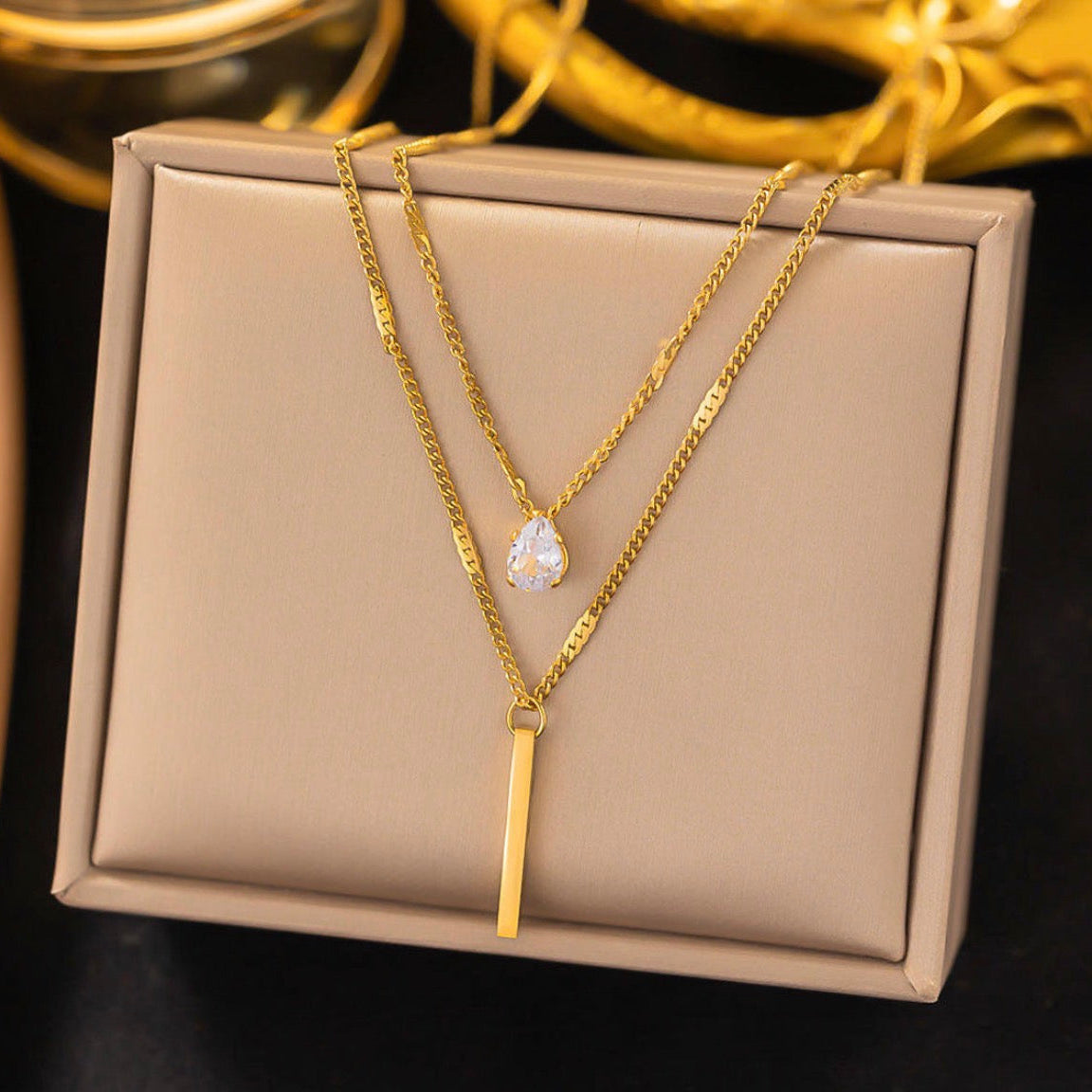 Gold necklaces on a beige jewelry box with a blurred gold ring in the background.