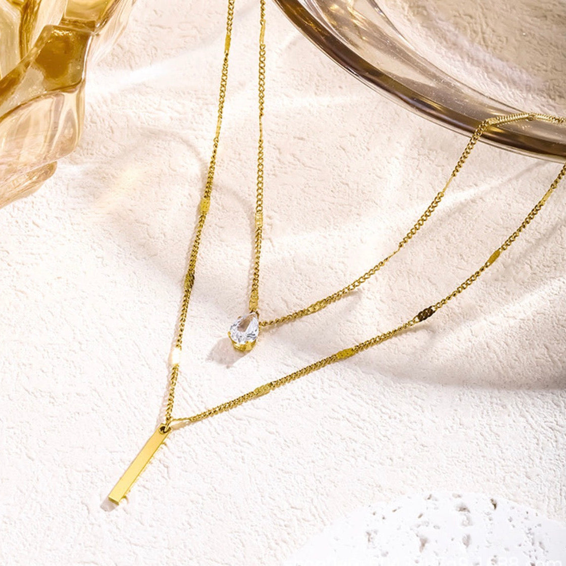 Two gold necklaces with small pendants on a white surface