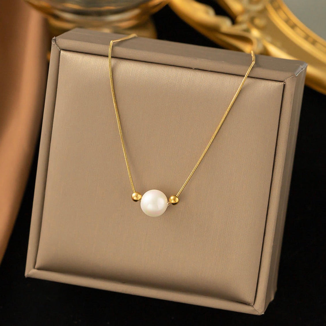 Gold necklace with a pearl pendant on a beige jewelry box