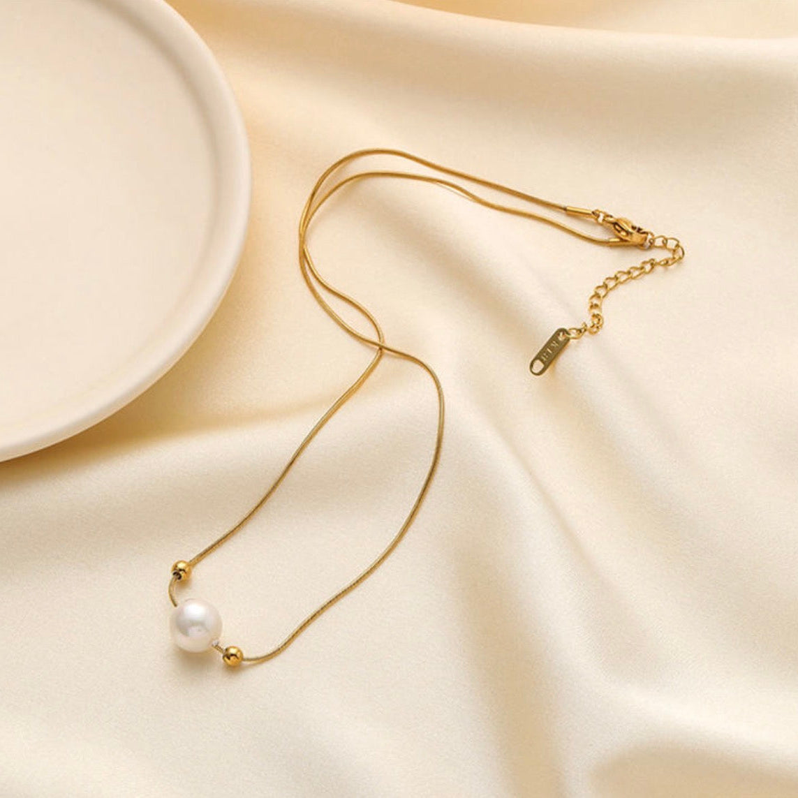 Gold necklace with a pearl pendant on a beige fabric background