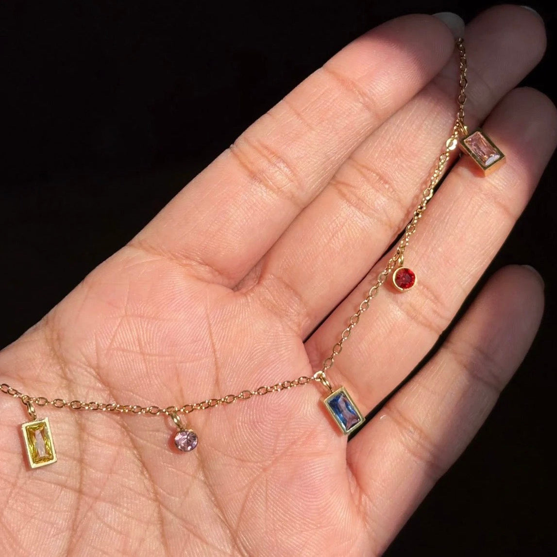 Gold chain bracelet with gemstone pendants on a hand against a black background