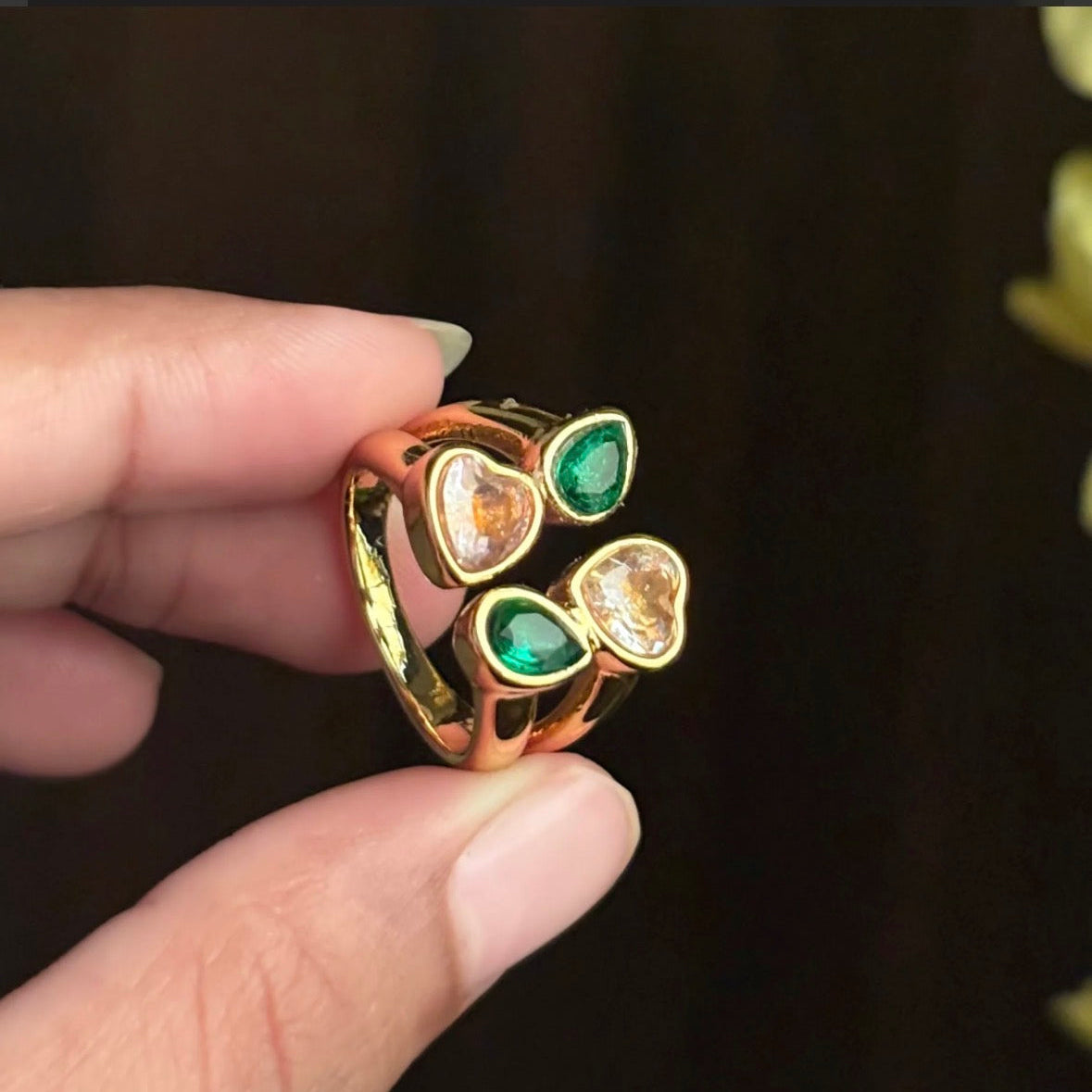 Gold ring with green and orange gemstones held by a hand against a dark background