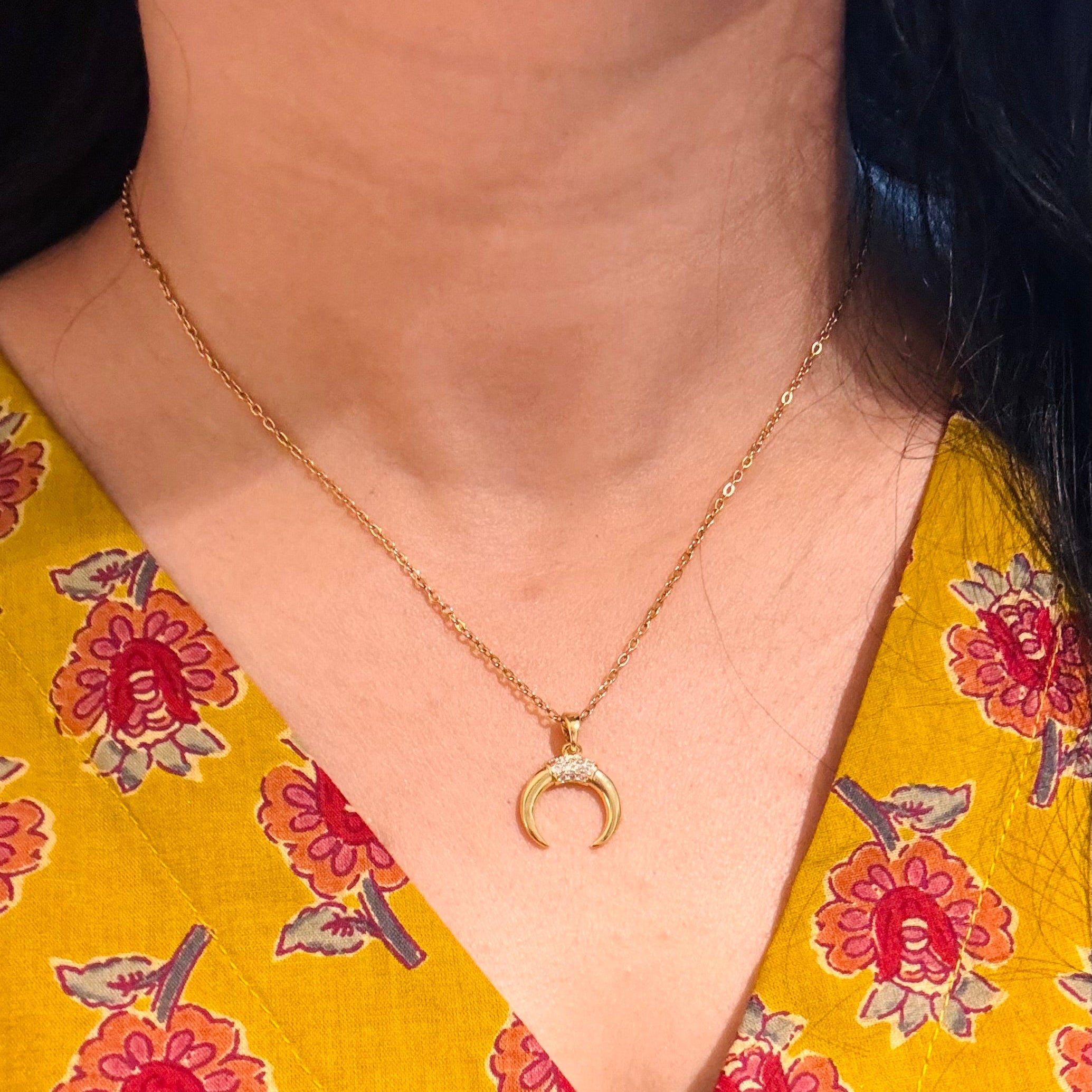 Person wearing a gold necklace with a crescent moon pendant on a yellow floral shirt.