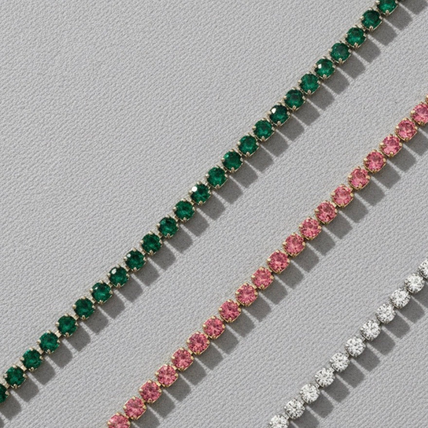 Three diamond bracelets with green, pink, and white stones on a light gray background