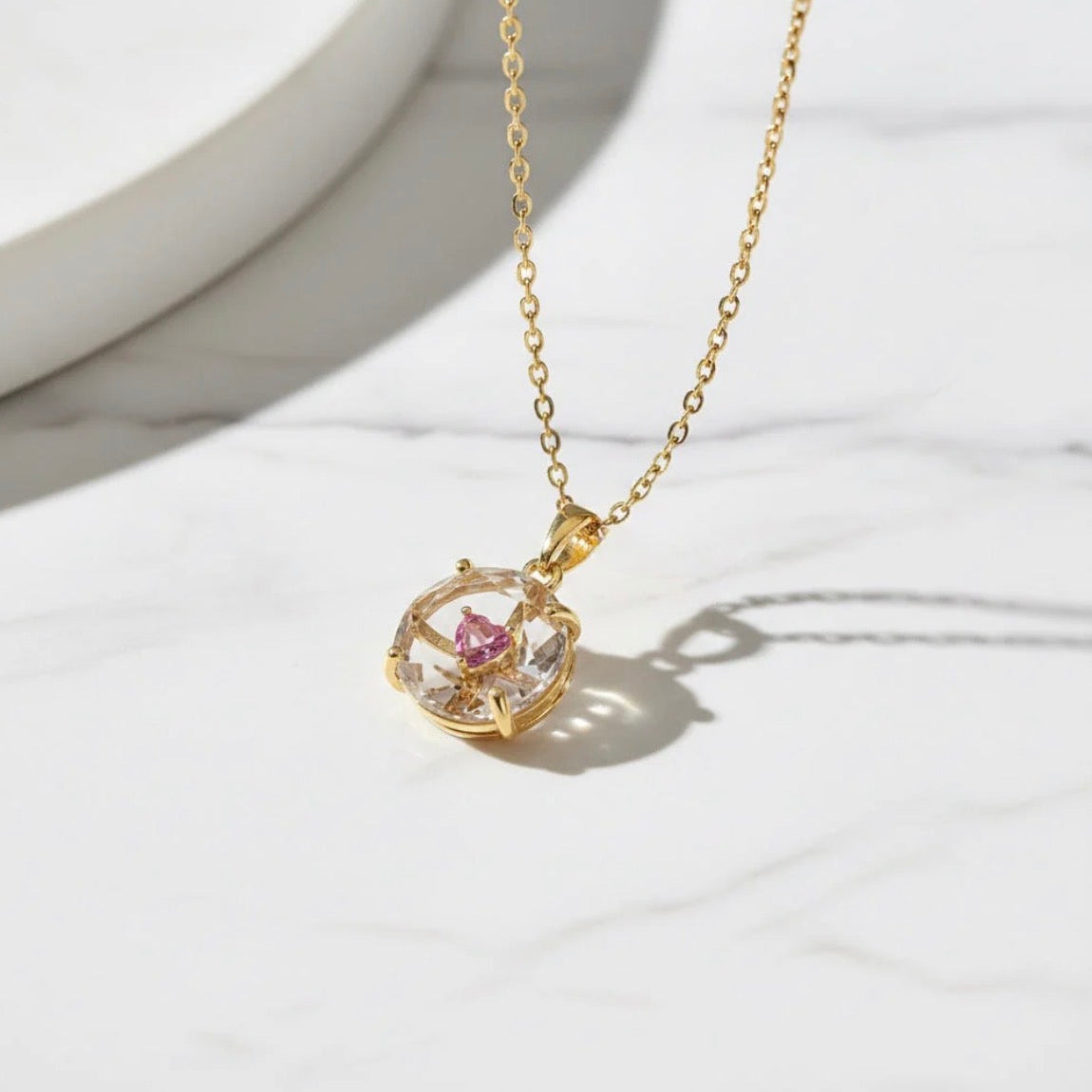 Gold necklace with a pink gemstone pendant on a white marble surface
