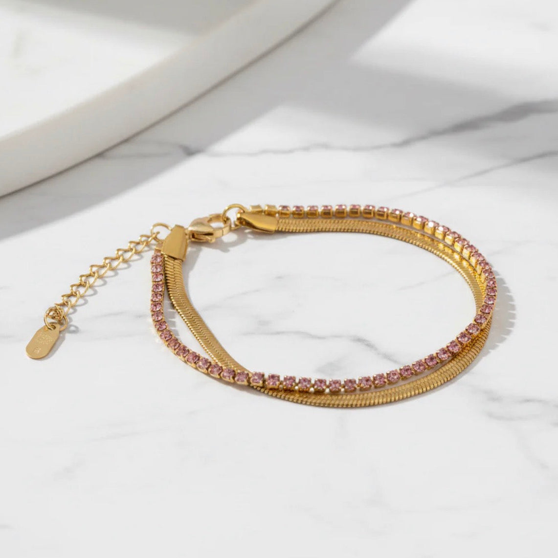 Gold bracelet with pink gemstones on a white marble surface