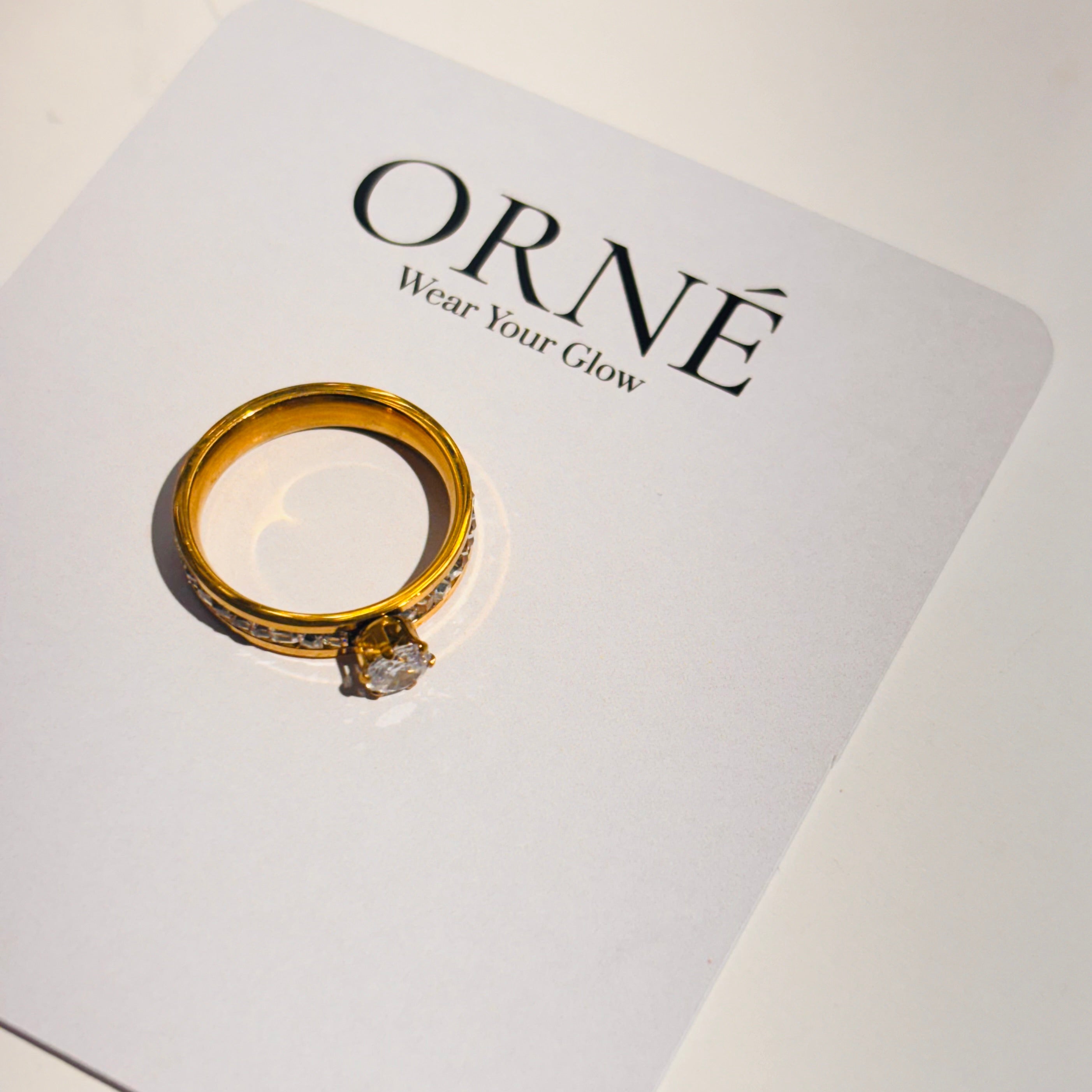 Gold ring on a branded card with 'Orne' and 'Wear Your Glow' text.