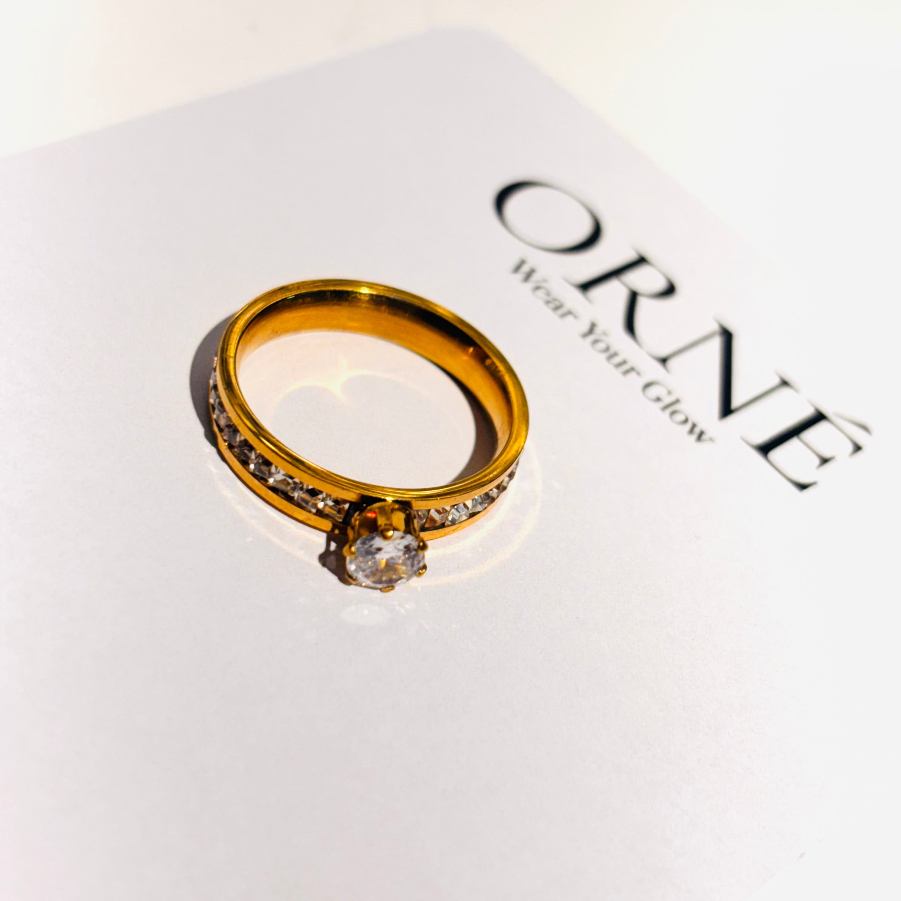 Gold ring with a diamond on a white box with 'ORNE' branding.