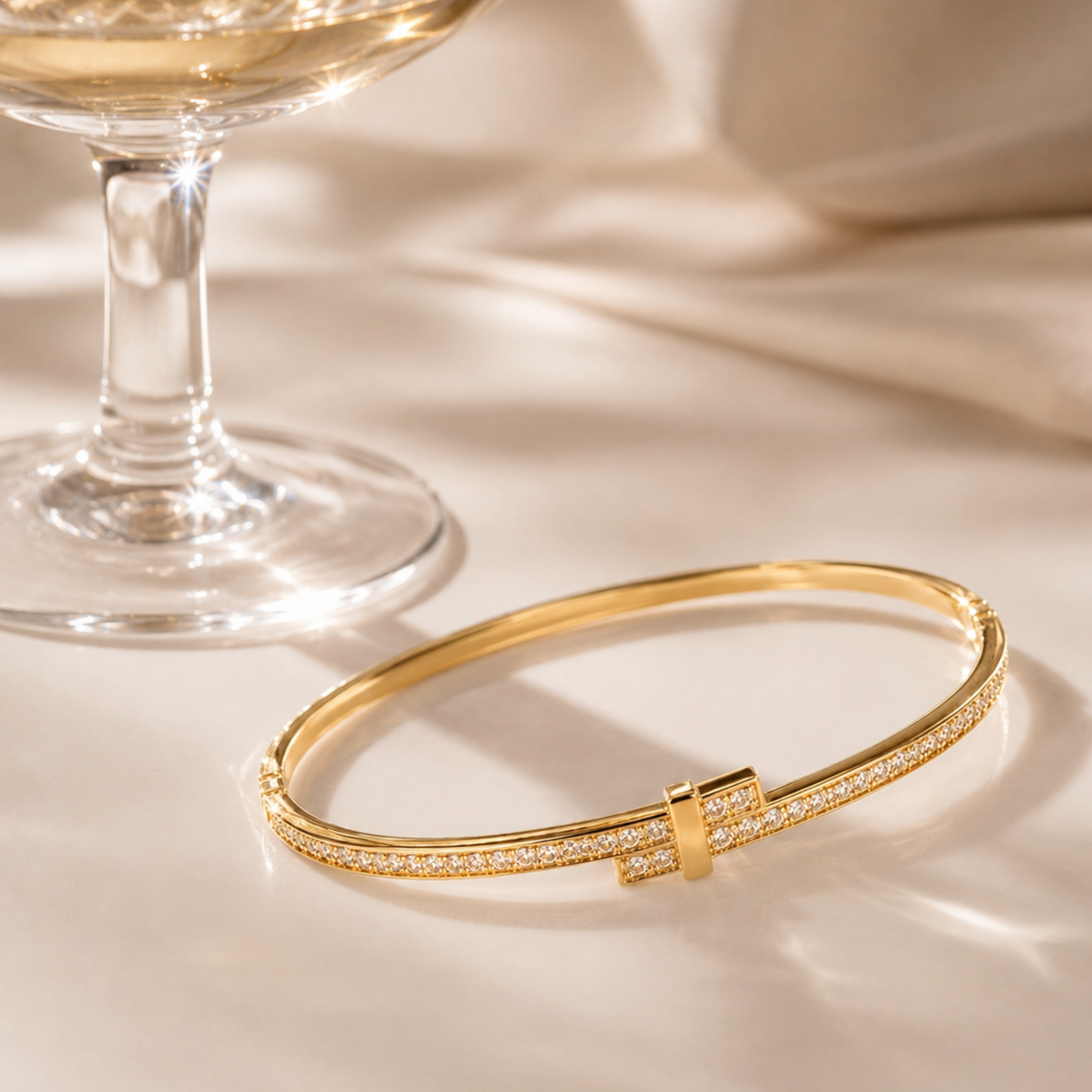 Gold bracelet on a reflective surface with a glass of white wine in the background