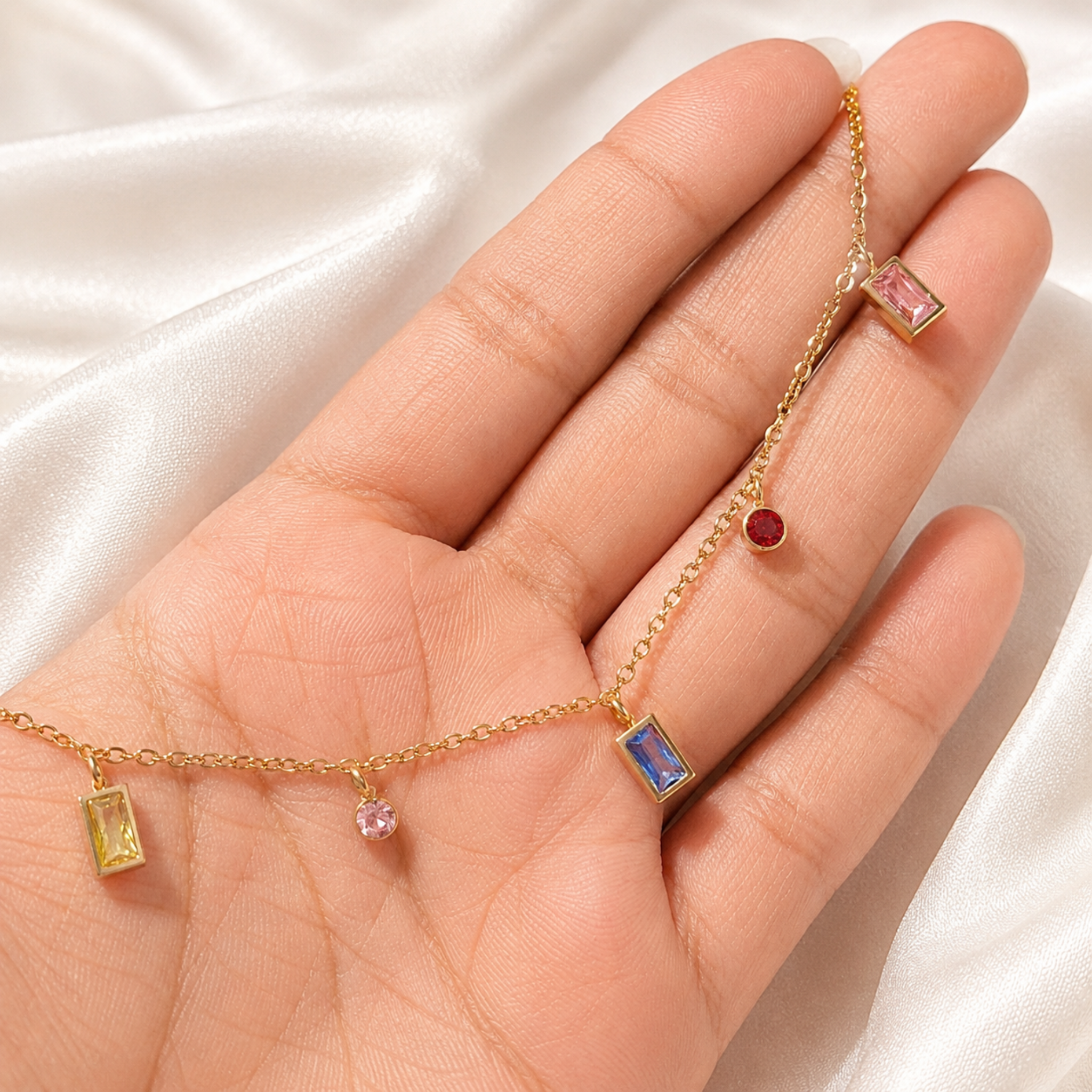Gold bracelet with gemstone charms on a hand against a white fabric background