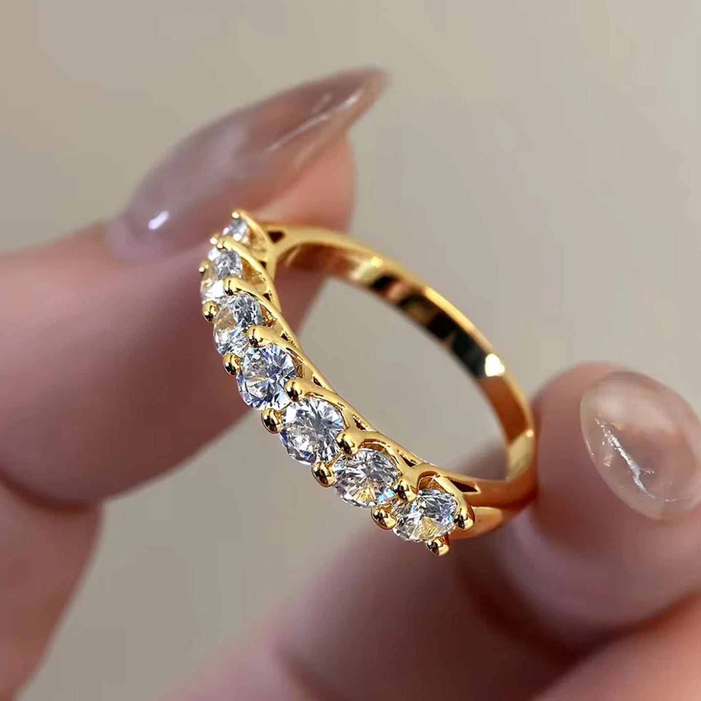 Gold ring with clear stones held by a hand against a neutral background