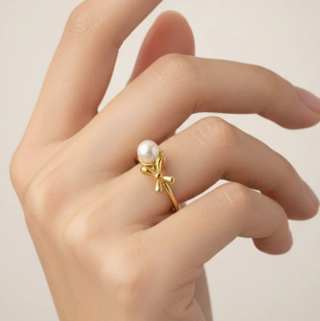 Gold ring with a pearl on a hand against a neutral background