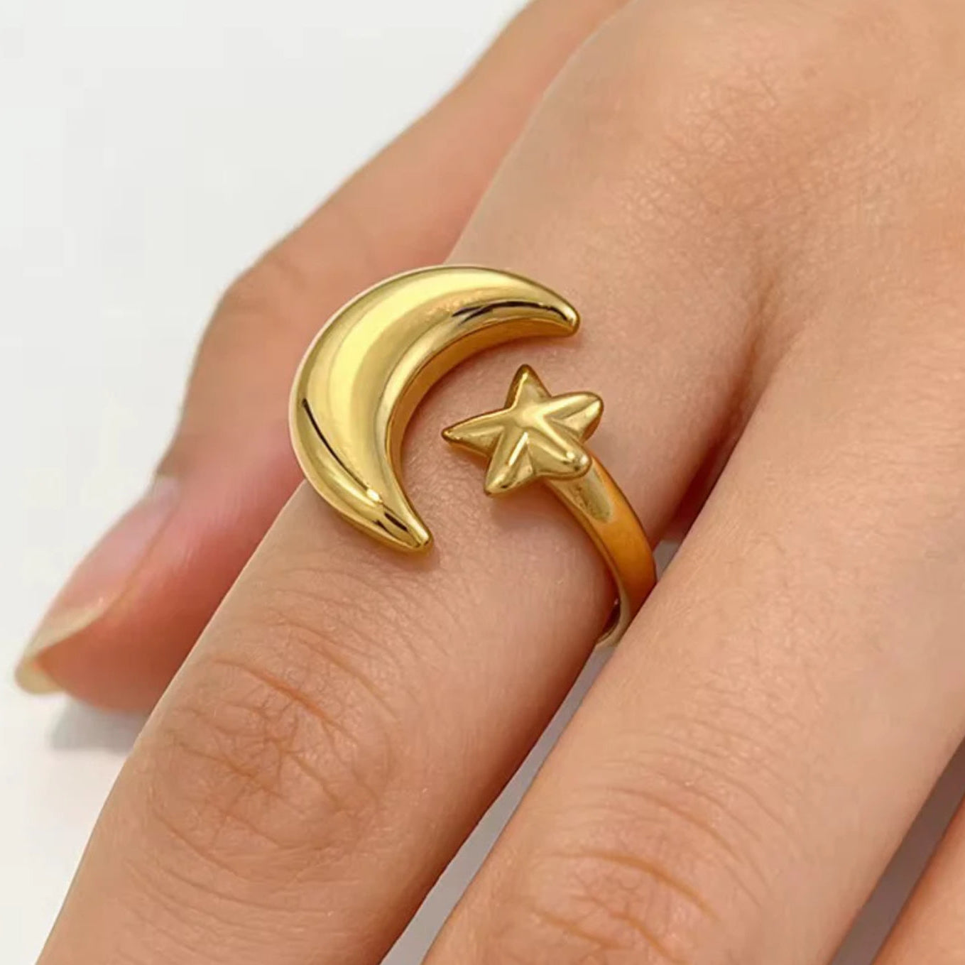 Gold ring with moon and star design on a finger against a white background