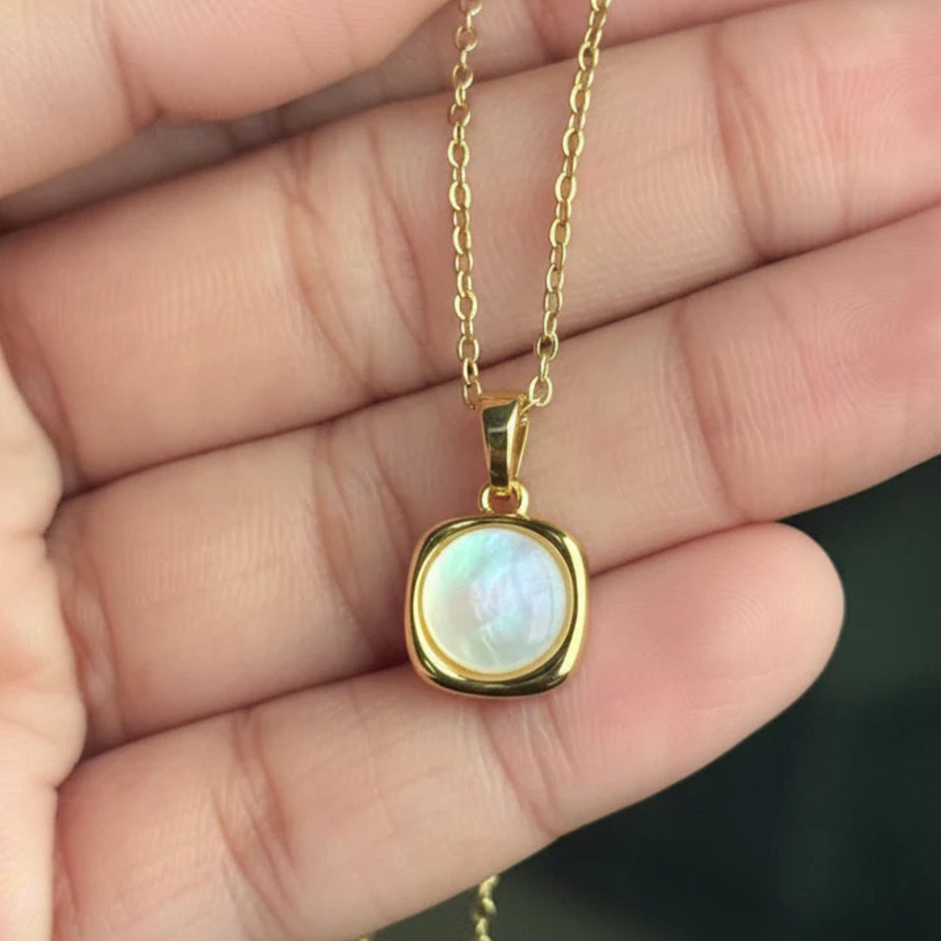 Gold necklace with a pendant held in a hand against a neutral background
